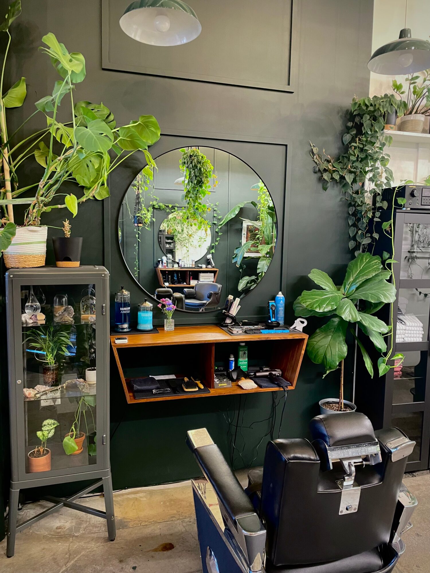 Salon station with mirror, plants, and a black chair in a green-themed room.