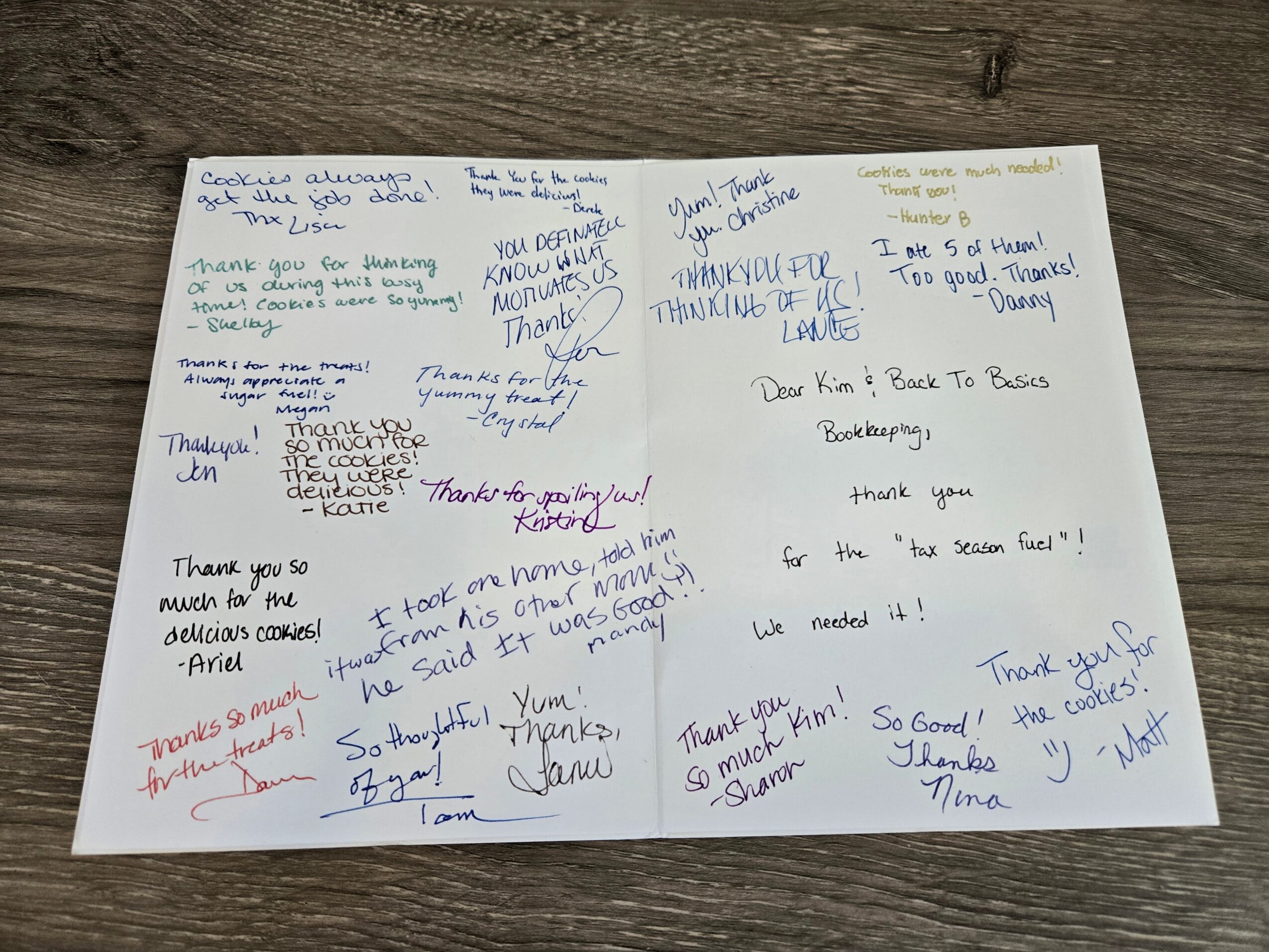 Handwritten notes and messages on a white paper, with some words highlighted in blue and red ink, placed on a wooden surface.