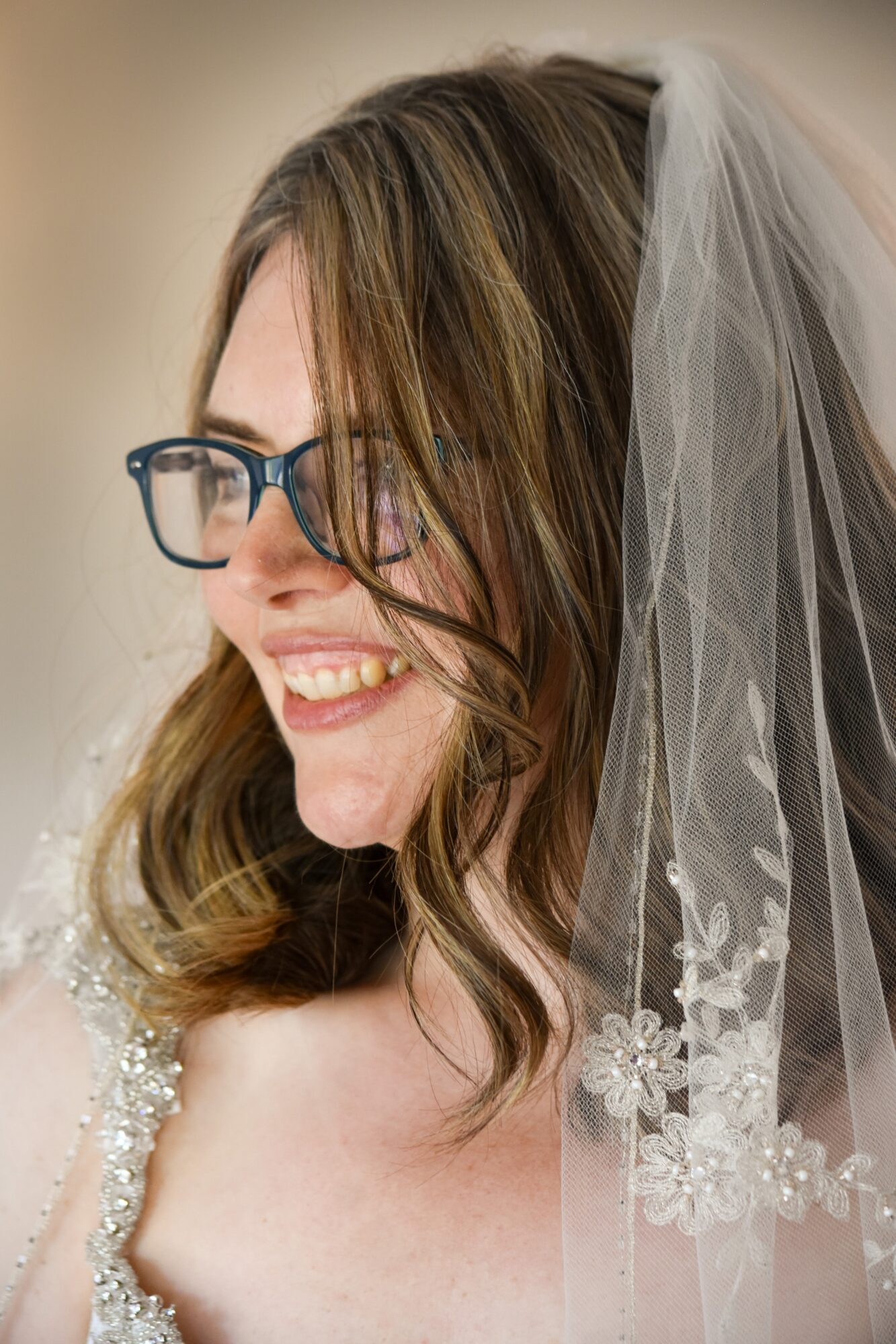 Woman with glasses and a veil, smiling, with wavy hair and floral details on her dress
