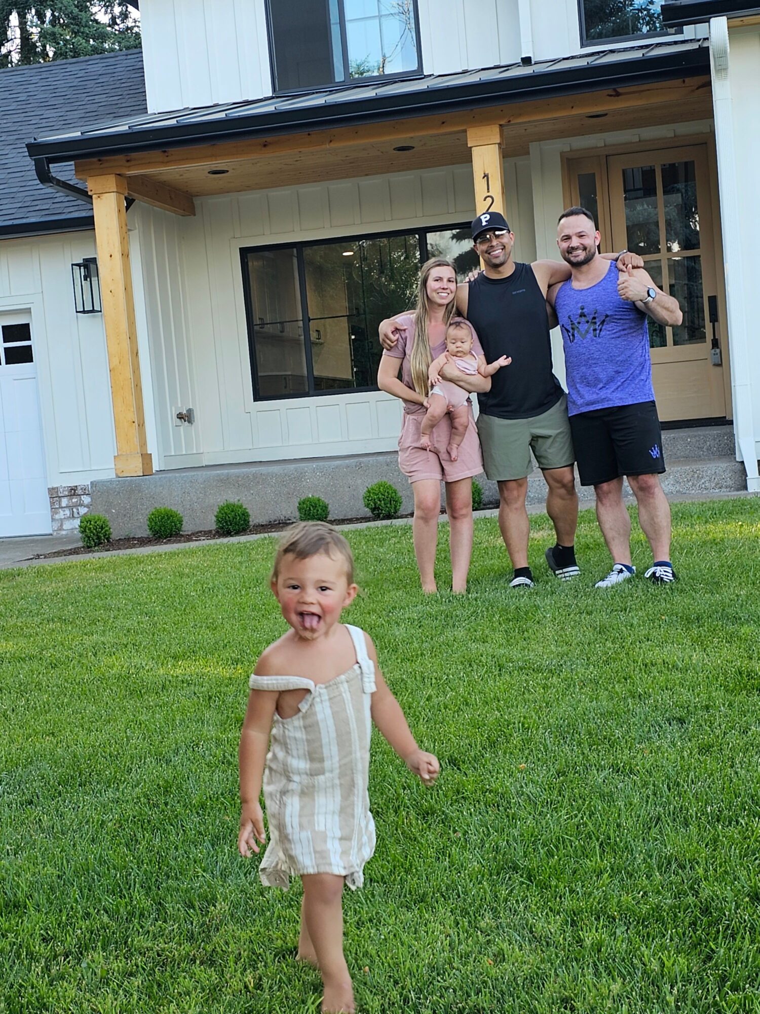 Four people, including children, standing on a lawn in front of a house, with one child in the foreground and three adults in the background.