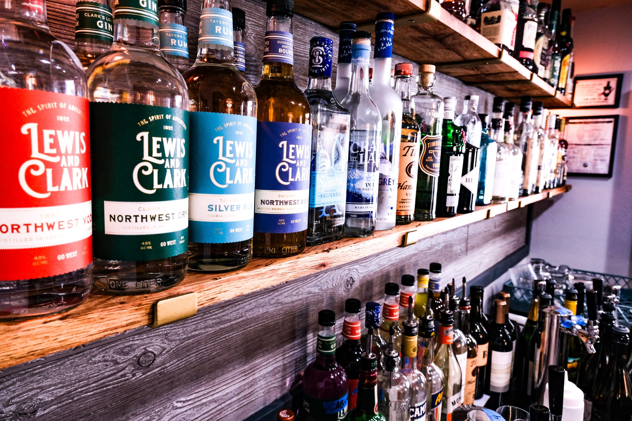 Bottles of Lewis Clark whiskey on a wooden bar shelf with other bottles in the background.