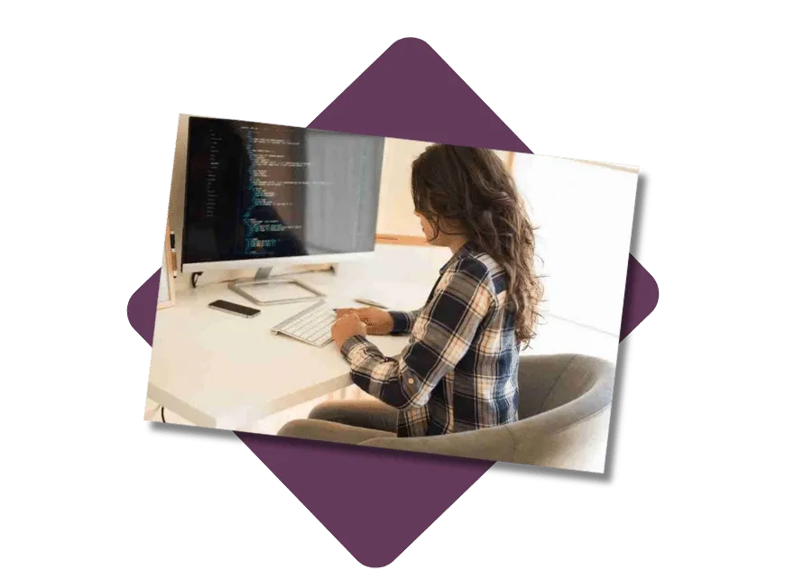 Person working at a desk with a computer, wearing a plaid shirt, in a bright room.