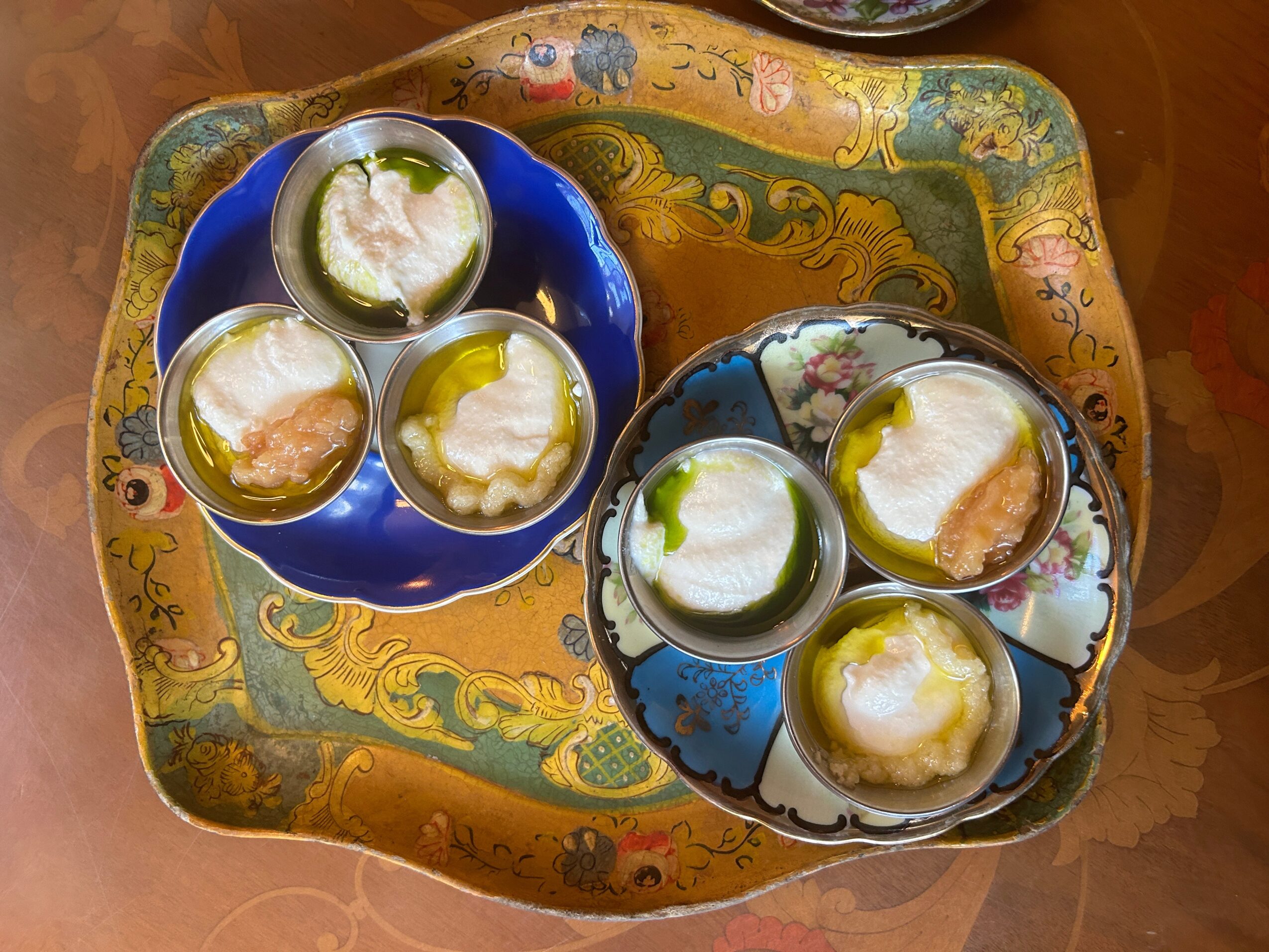 Four small desserts with green garnish on two colorful plates, placed on a decorative tray with intricate patterns.
