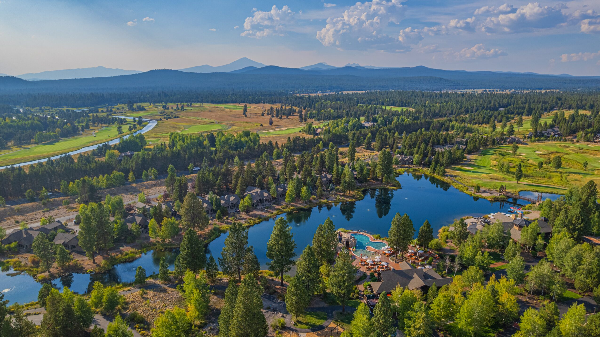 Landscape with lakes, trees, houses, and distant mountains under a partly cloudy sky.