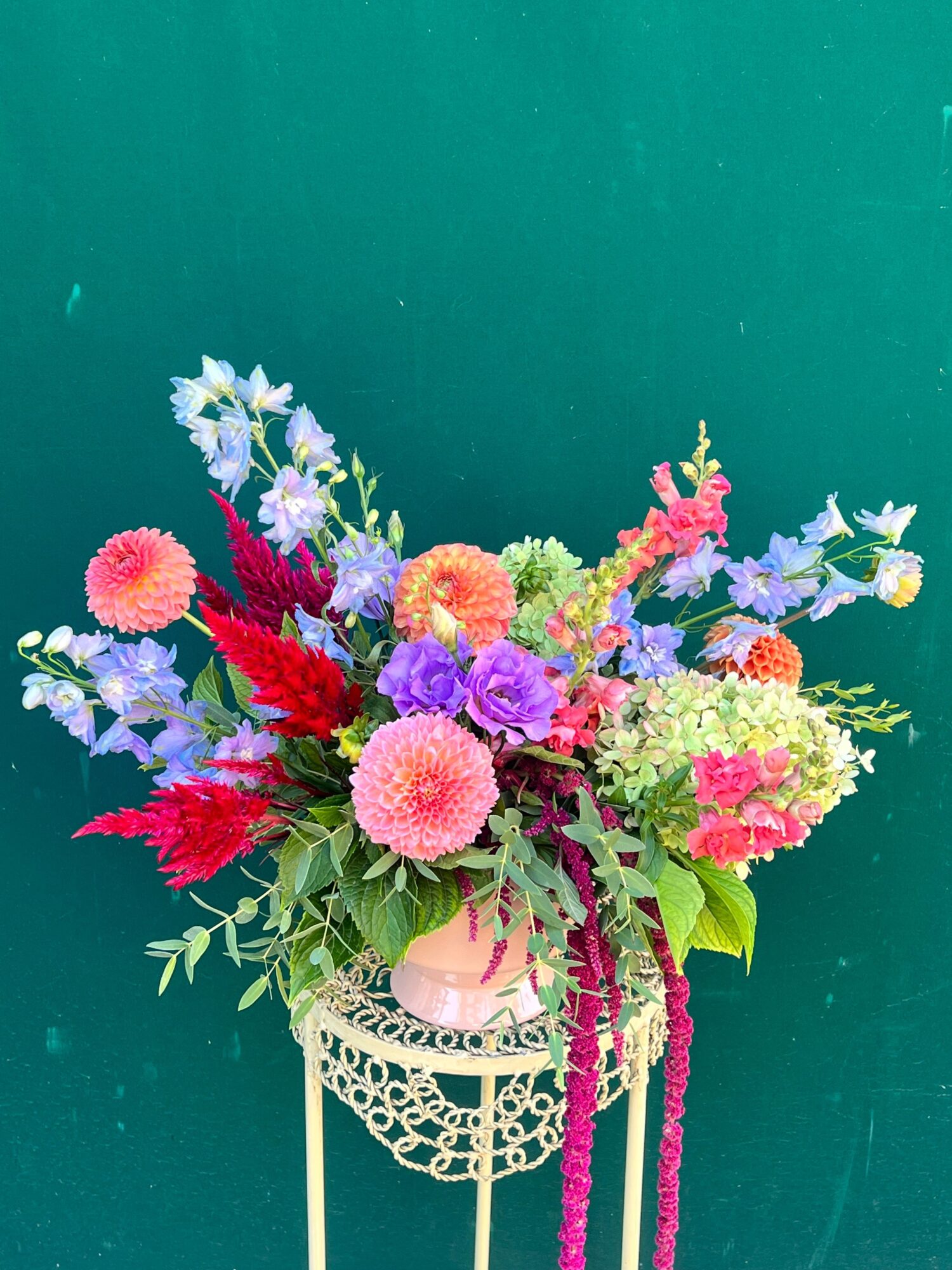 Colorful bouquet of flowers with pink, purple, red, and white blooms against a teal background.