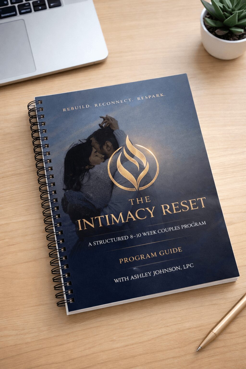 Book titled 'The Intimacy Reset' on a wooden desk with a laptop, potted plant, and gold pen nearby.