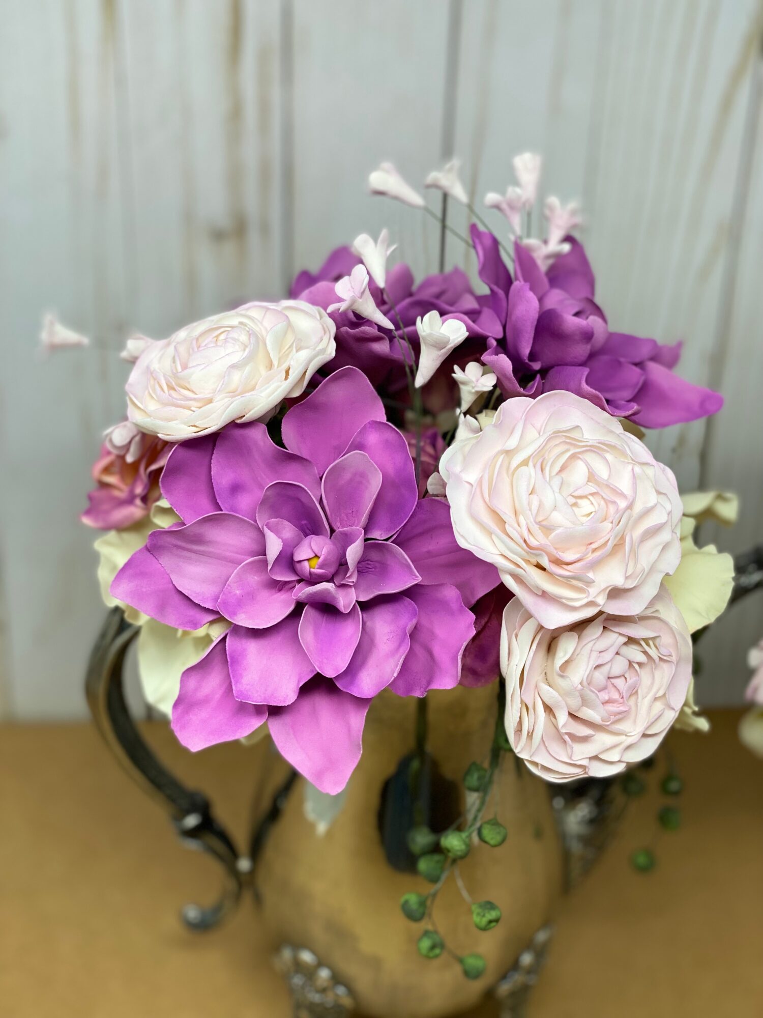 Flower arrangement with purple and white flowers in a beige vase, against a light background.