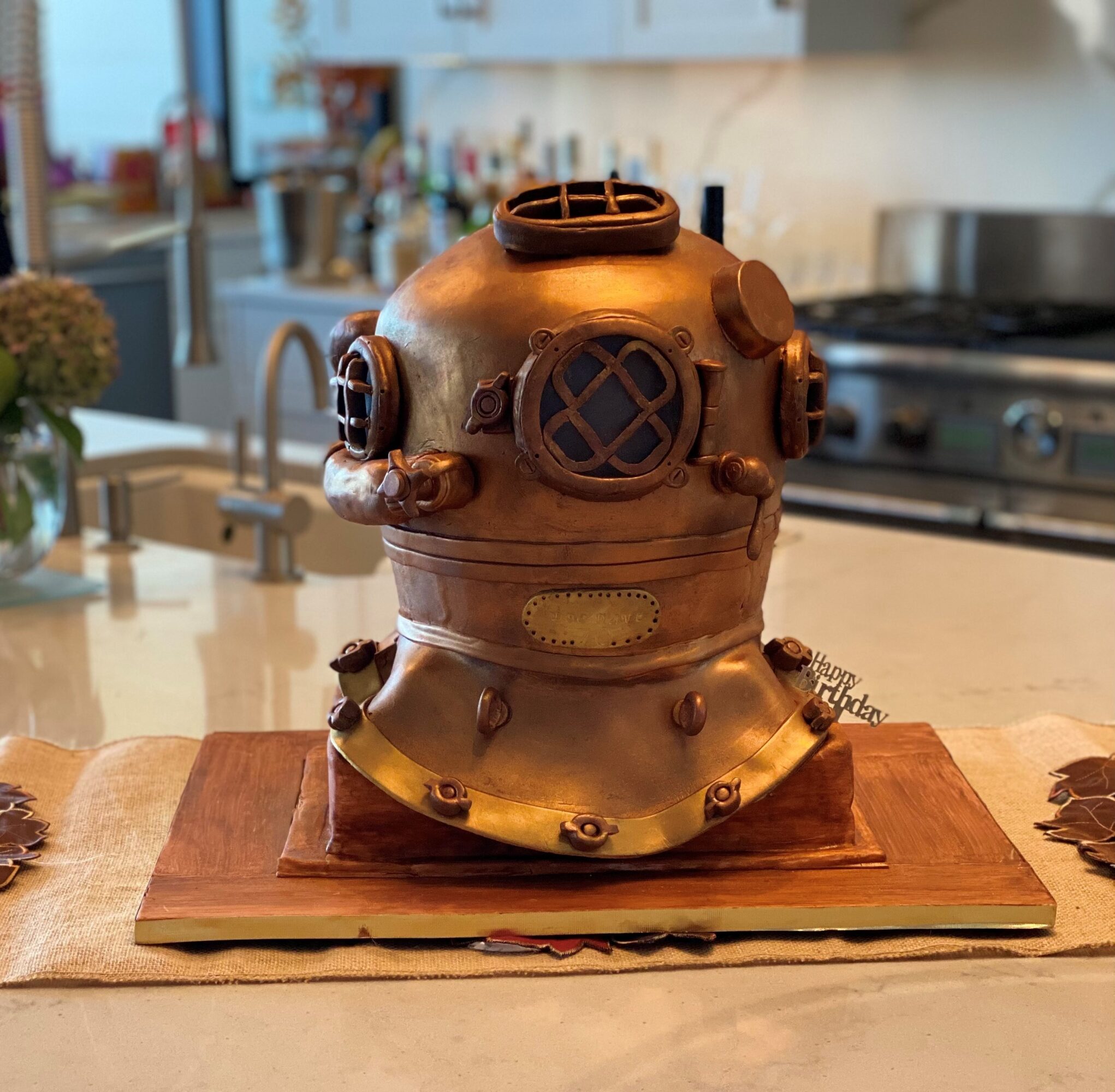 Steampunk-style cake shaped like a vintage diving helmet on a wooden base, in a kitchen setting.