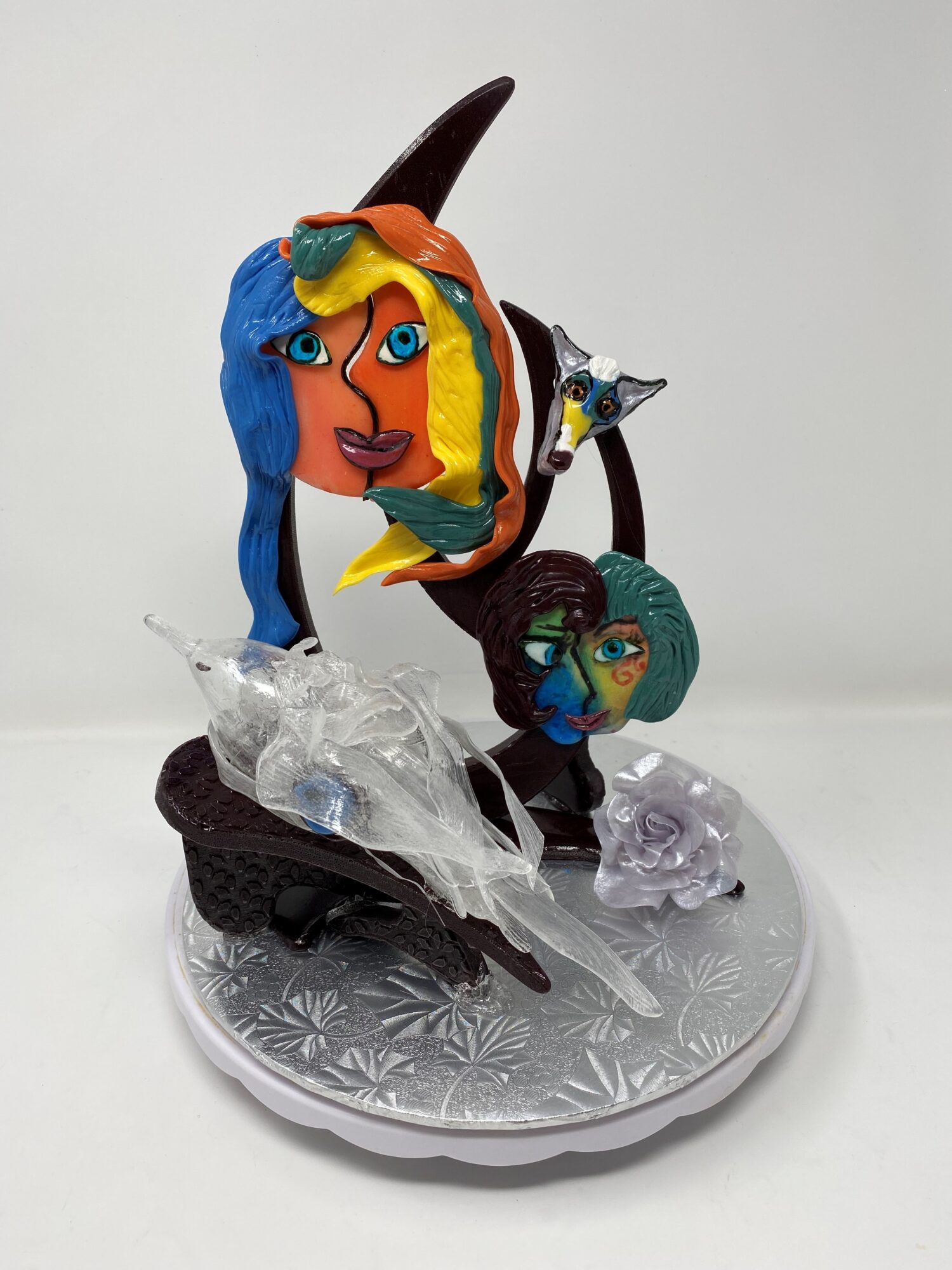 Colorful sculpture of a woman with blue hair, a small bird, and a face, on a decorative base.