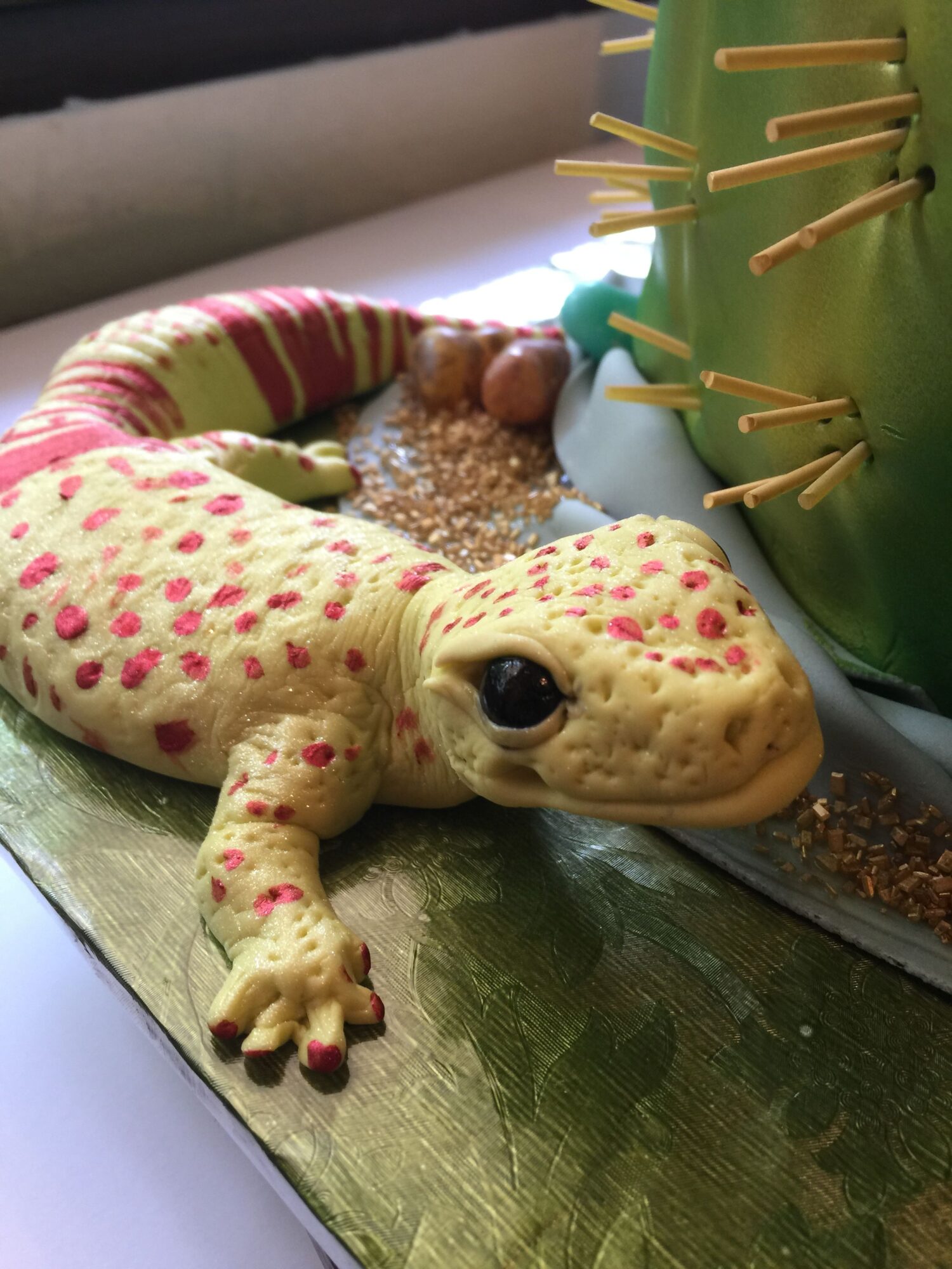 A toy or model of a creature with a cream-colored body covered in pink spots, black eyes, and a small mouth, lying on a metallic surface.