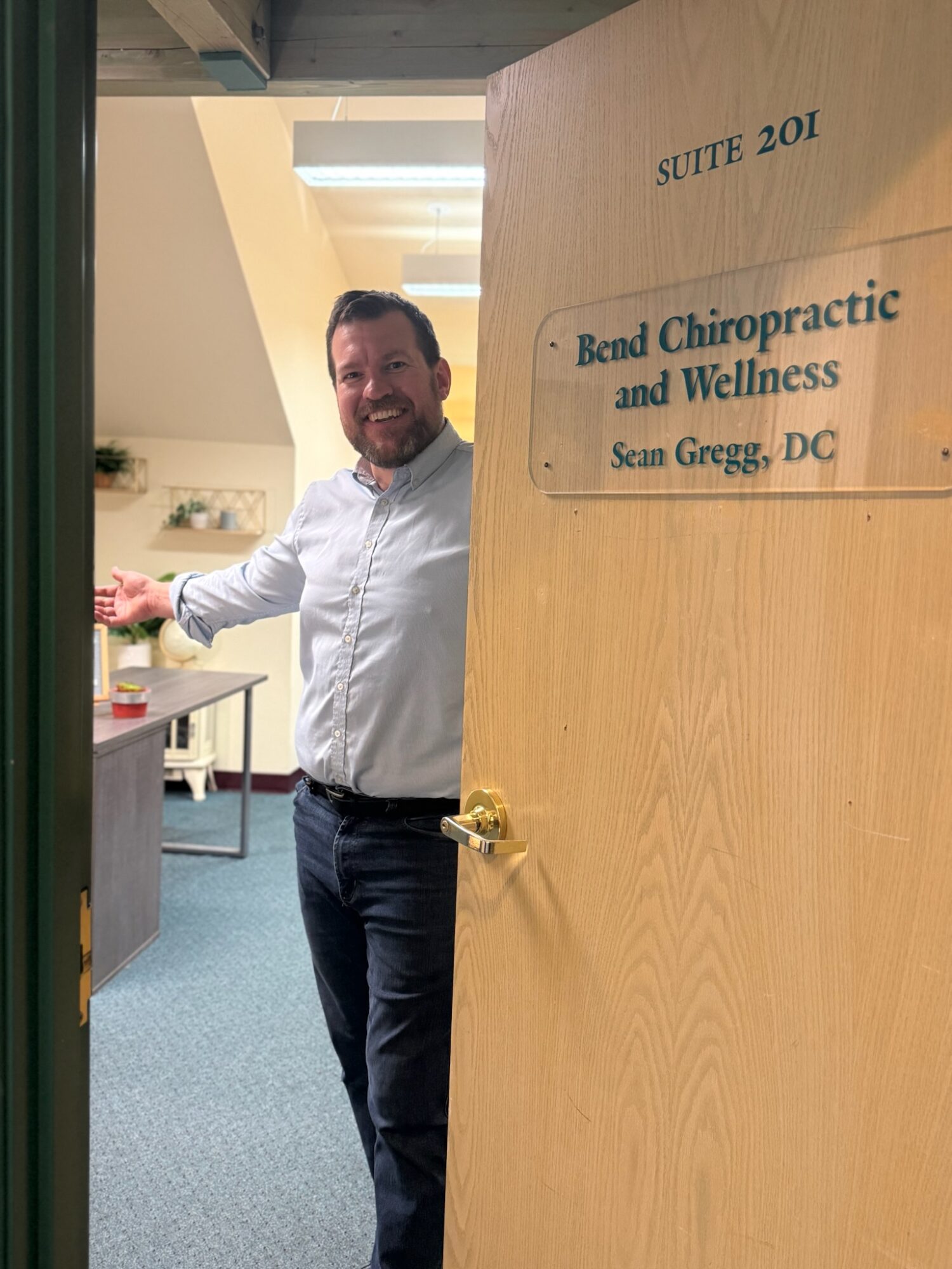 Man standing in doorway of chiropractic office, smiling, with sign reading 'Bend Chiropractic and Wellness, Sean Gregg, DC'.