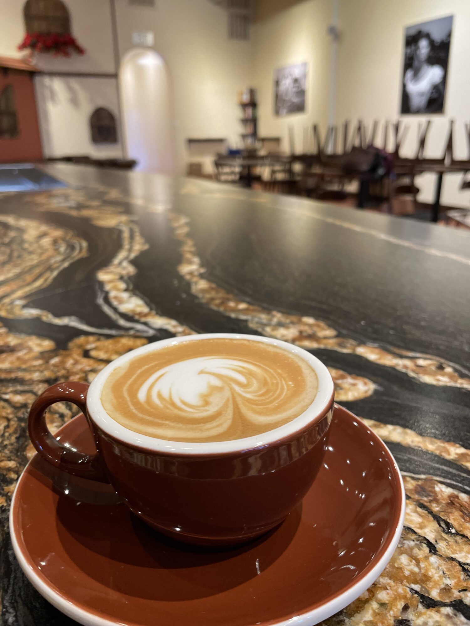 A cup of coffee with latte art on a marble table in a cafe, with artwork on the wall in the background.