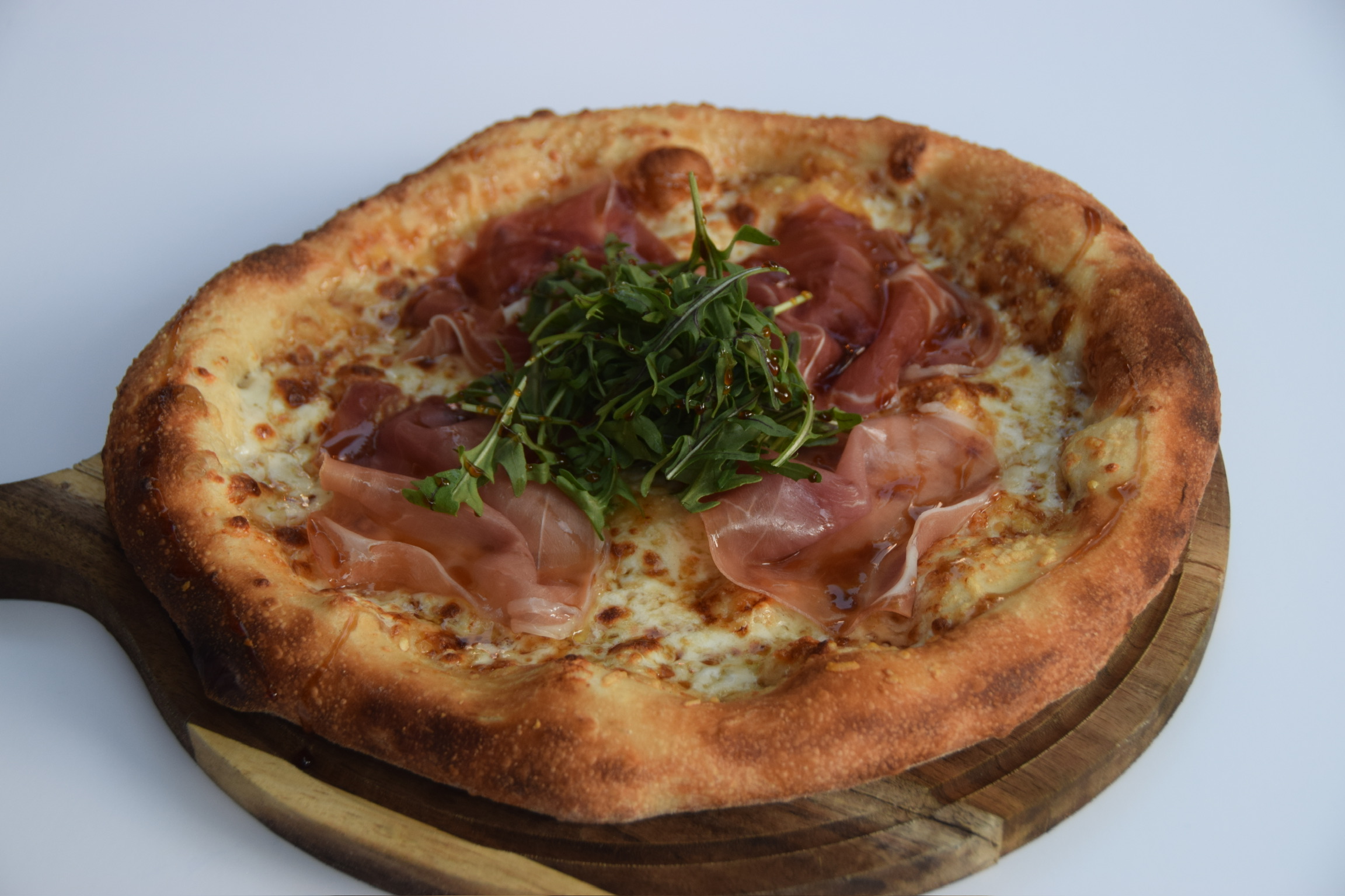 Pizza with ham and greens on a wooden board, viewed from above.