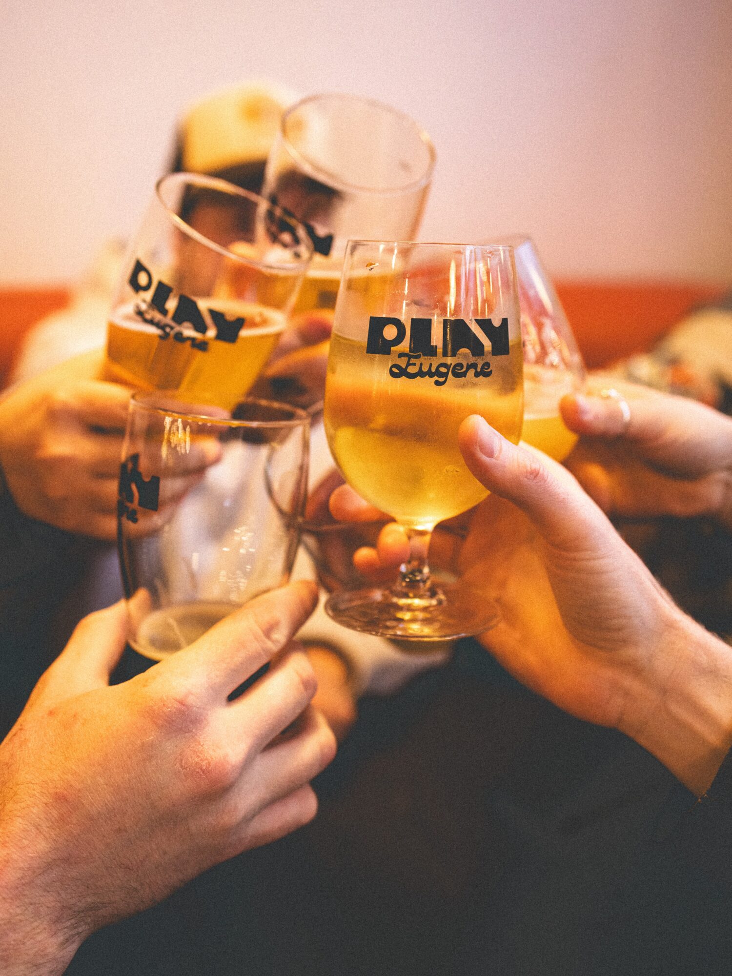 Four people clink glasses filled with beer, with a blurred background, celebrating together.