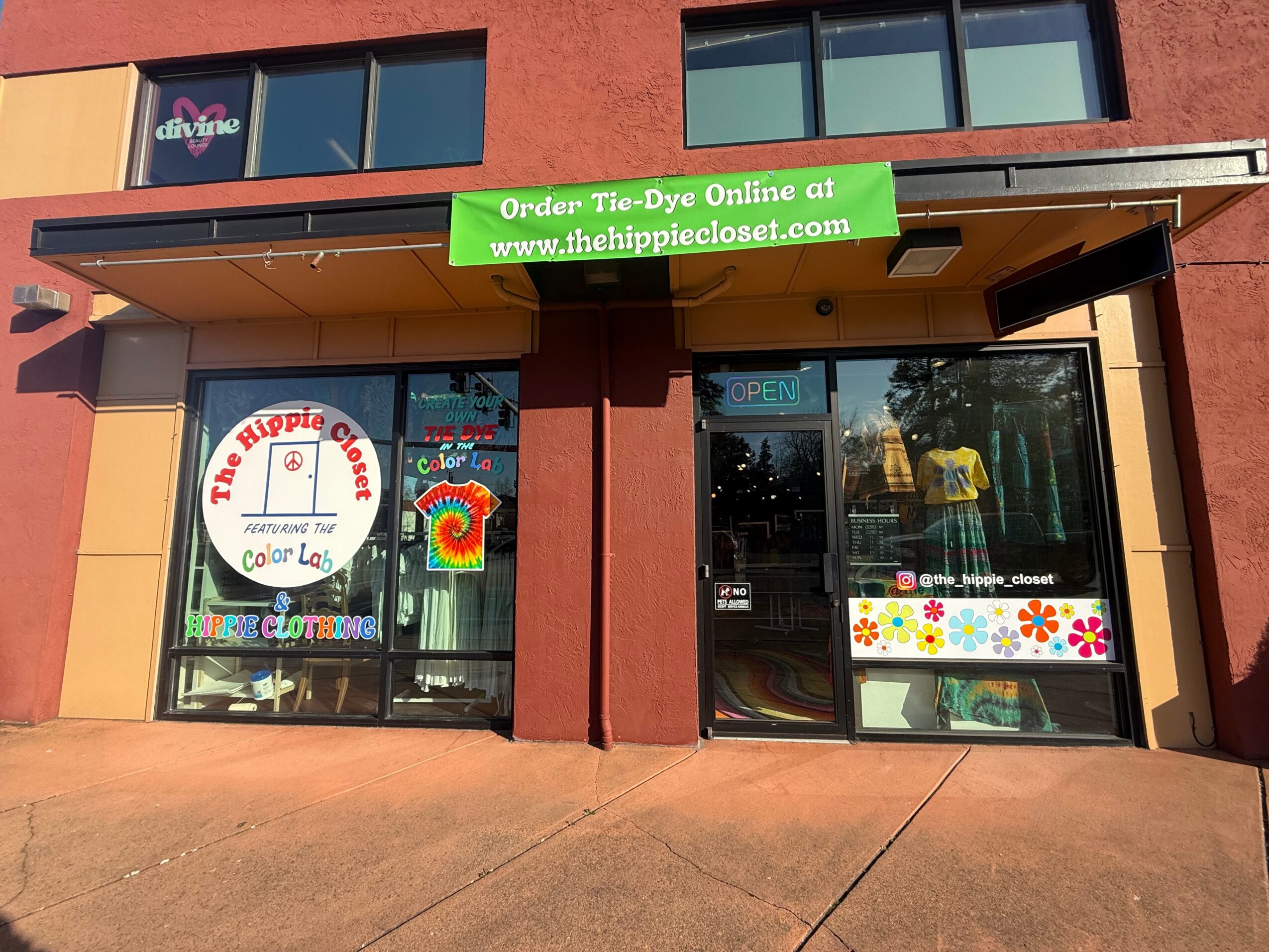Storefront with colorful signs and windows, one with a rainbow and flower decorations, and a green banner above.