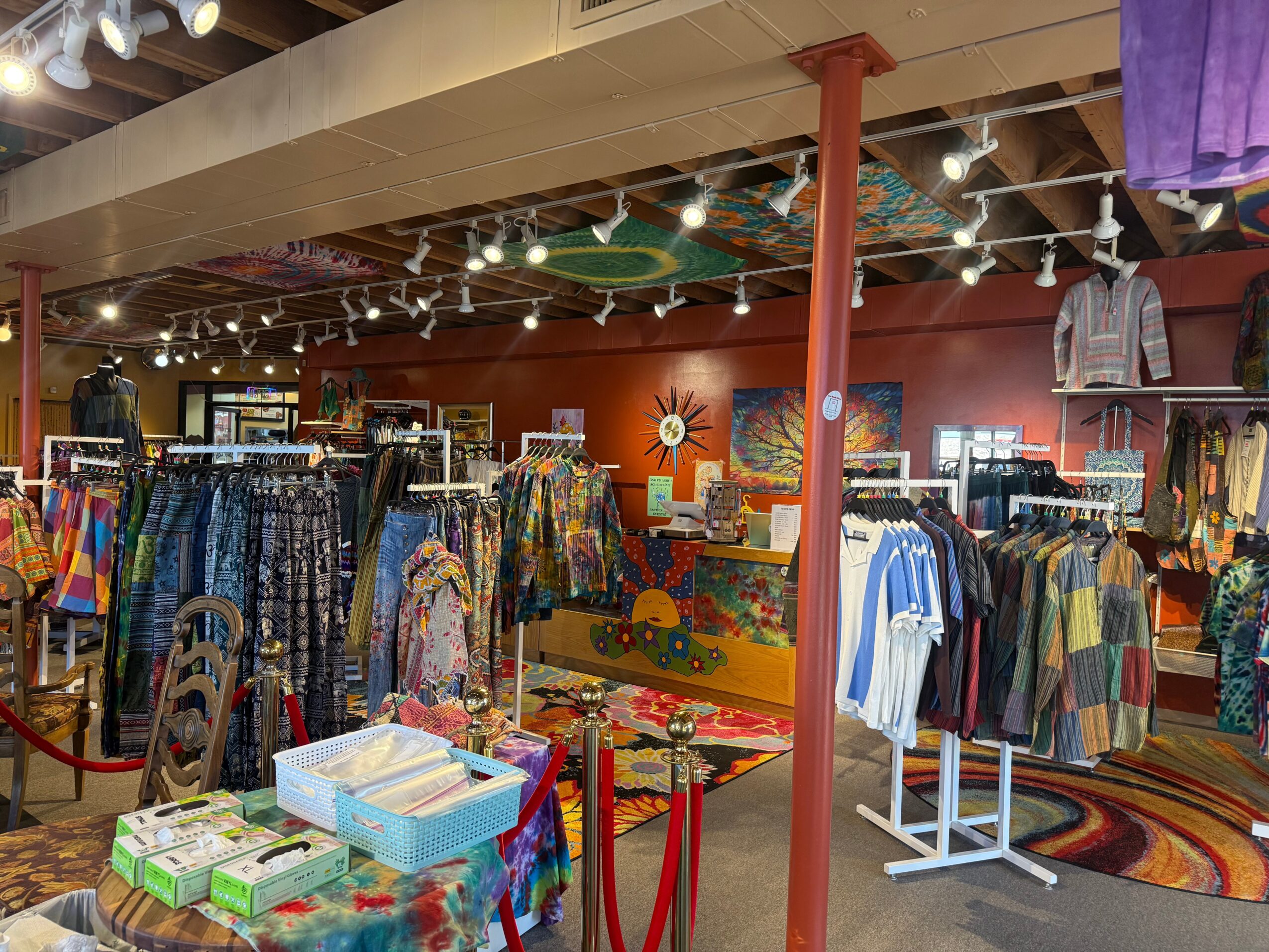 Clothing store interior with racks of colorful clothes, decorative wall art, and ceiling string lights.