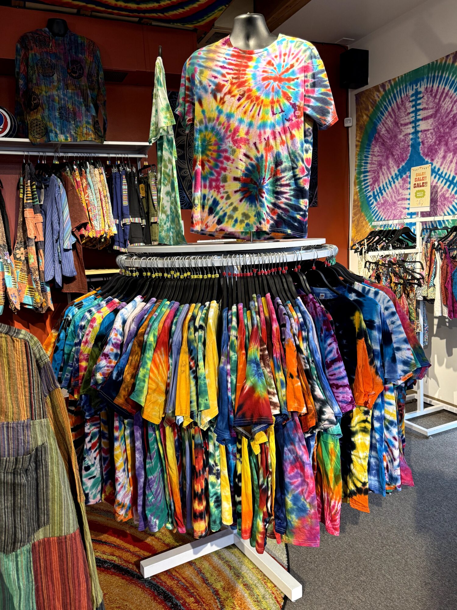 Display of colorful tie-dye T-shirts and clothing in a store, with a tie-dye wall hanging in the background.