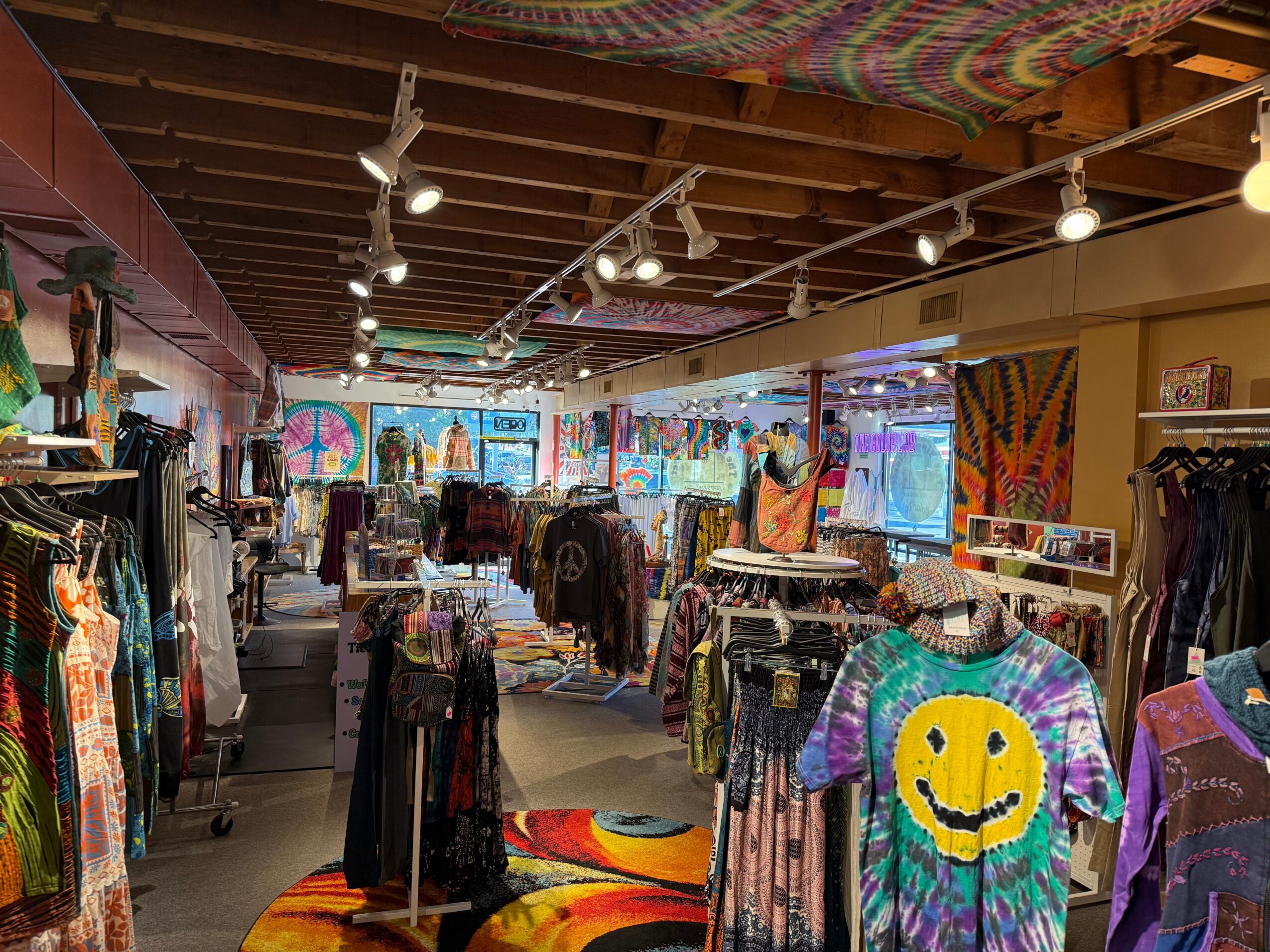 Clothing store interior with racks of clothes, colorful artwork, and bright lighting, viewed from the front entrance.