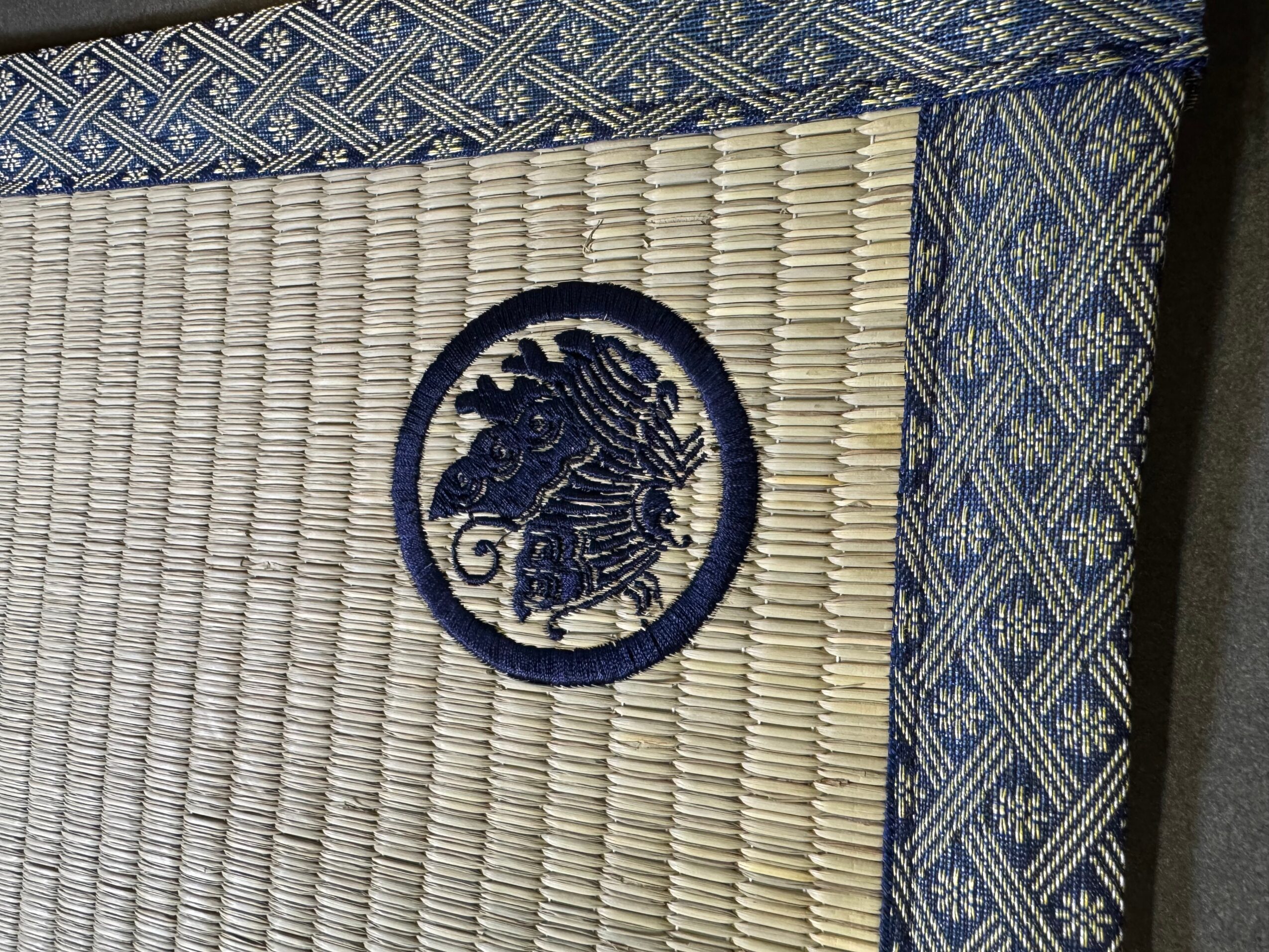 Close-up of a woven mat with a embroidered seahorse emblem and patterned fabric border.