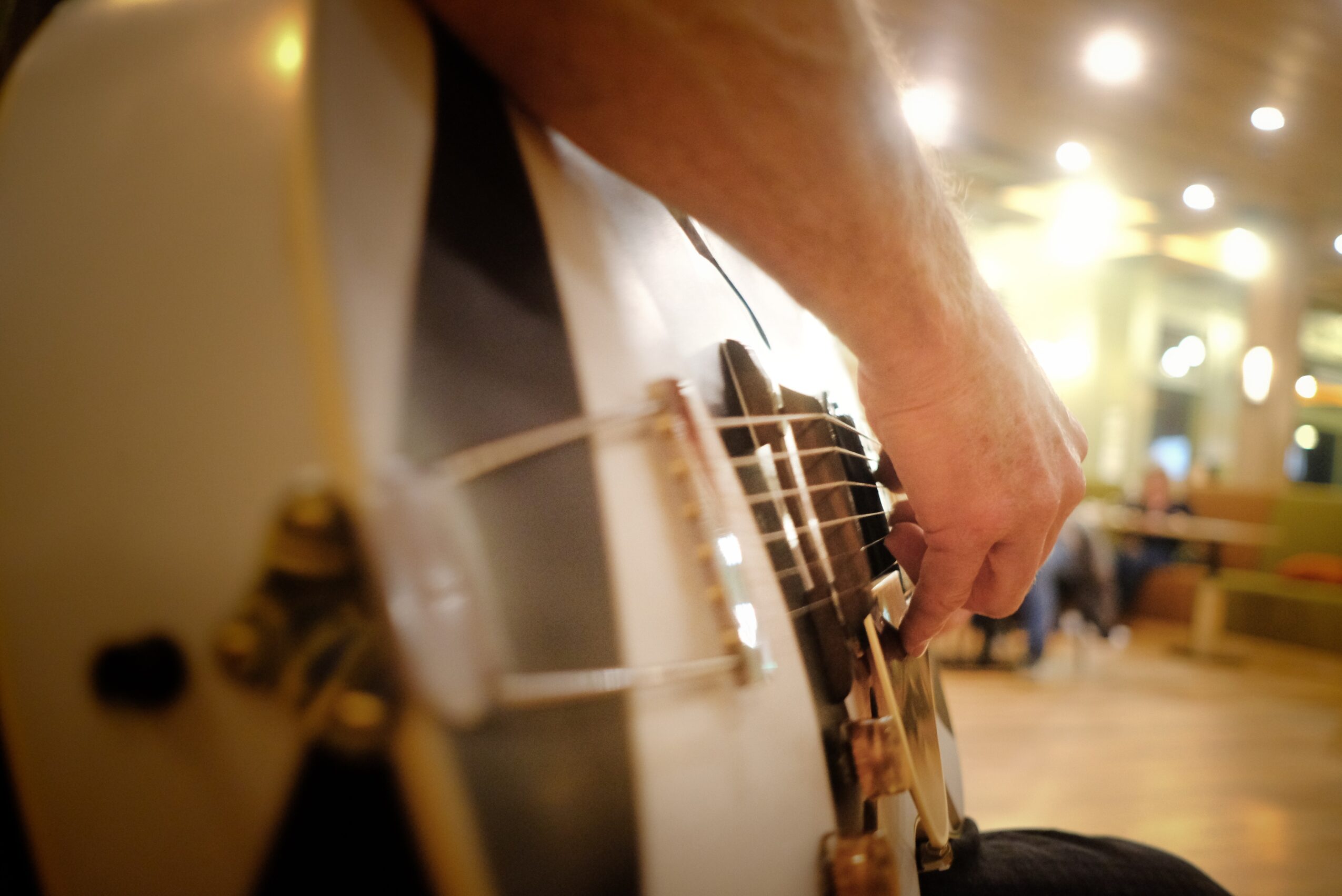 Close-up of a person playing an acoustic guitar in a room with warm lighting and blurred background.