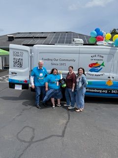 Group of five people standing outdoors near a white van with colorful balloons attached, on a paved surface.