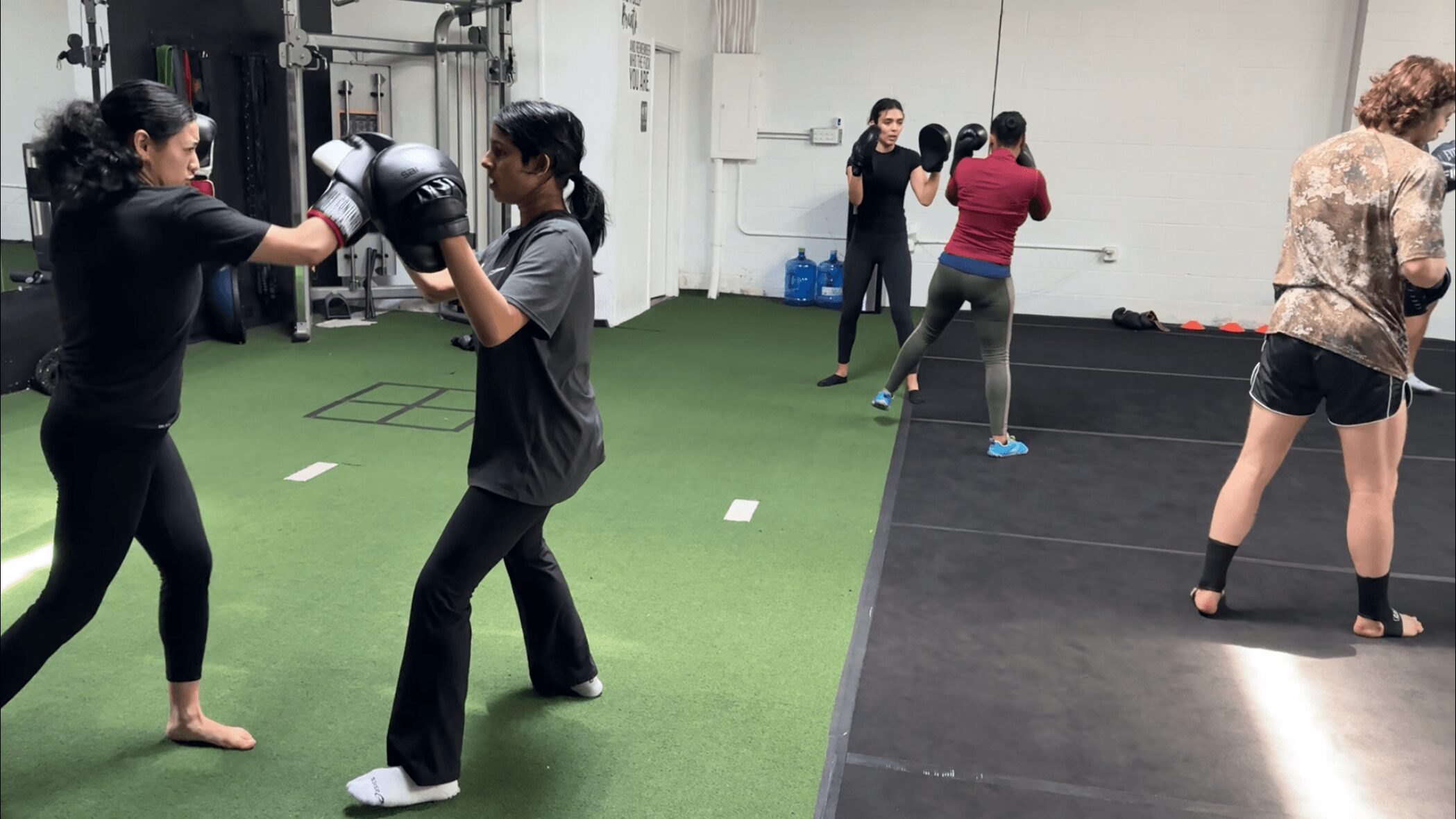 People practicing boxing and fitness exercises in a gym with green and black flooring.