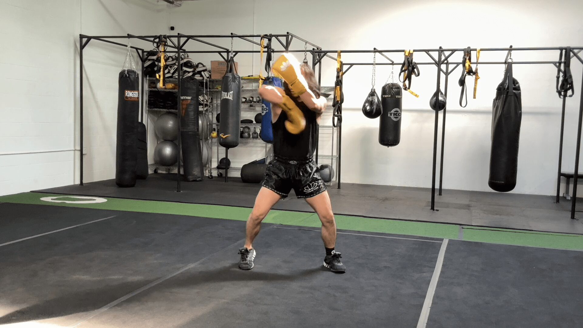 Person holding a medicine ball in a gym, standing on a black floor with workout equipment in background.