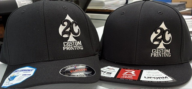Two black baseball caps with logo and text, displayed side by side on a surface.