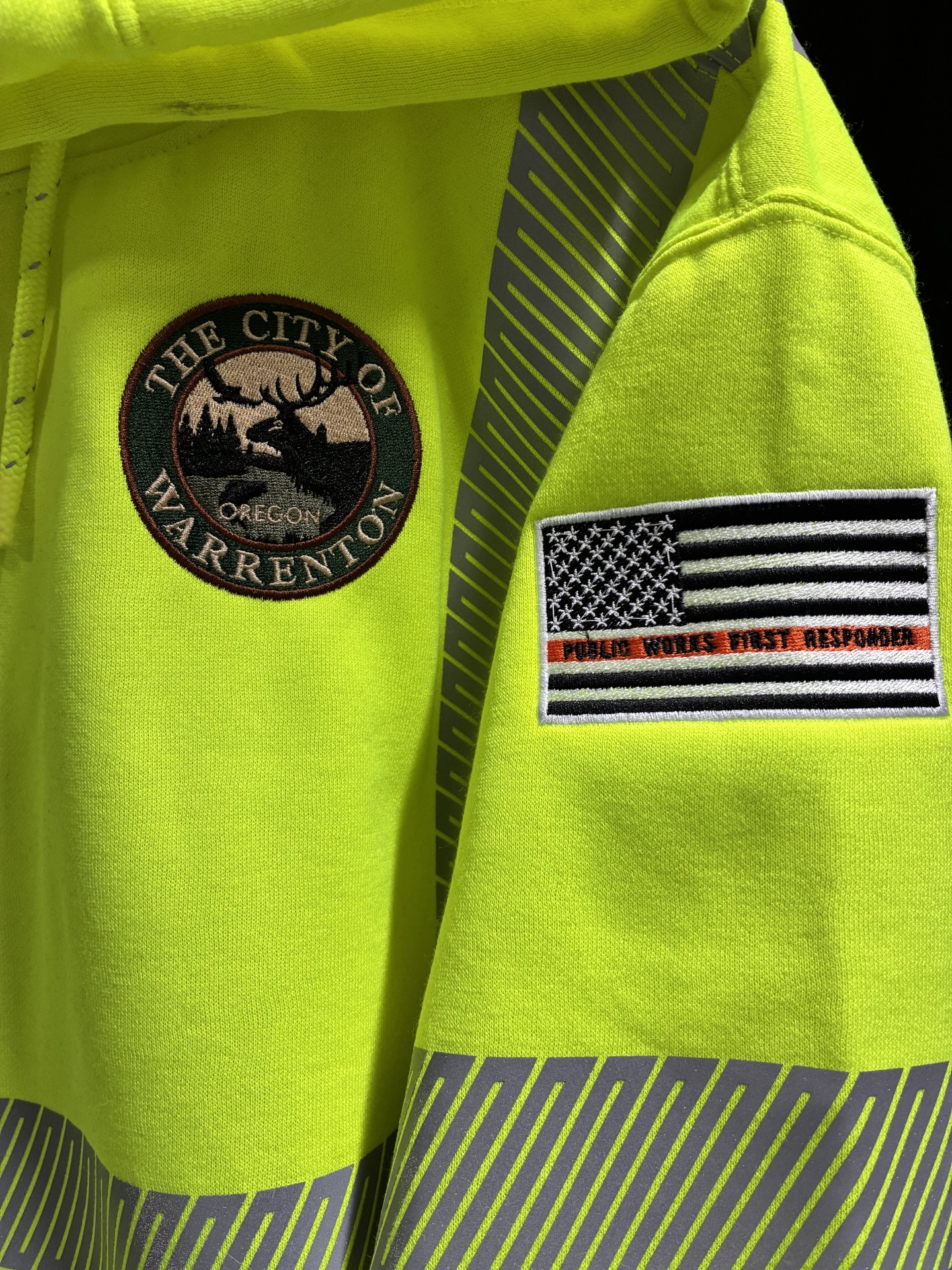 Close-up of a neon yellow jacket with patches, including a city emblem and a flag with a black and white American flag and red text.