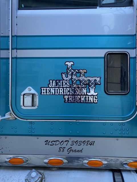 Truck door with logo and text, including a window and a small compartment, with a reflective surface and orange lights at the bottom.