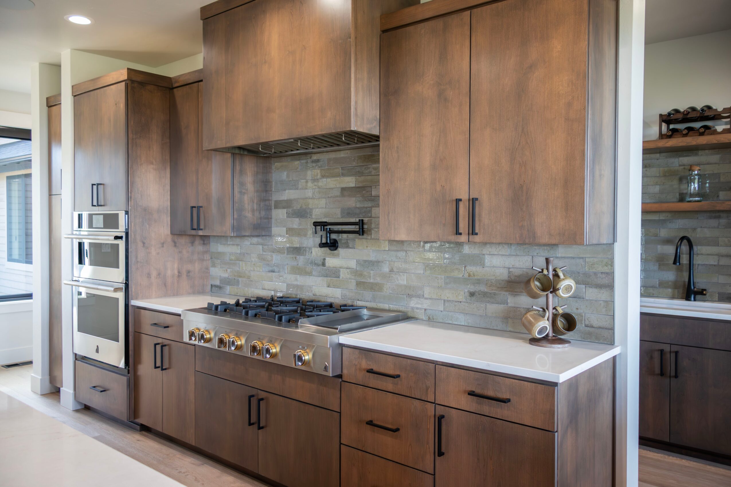Kitchen with wooden cabinets, a stove, and a gray backsplash, with a sink and faucet visible on the right.