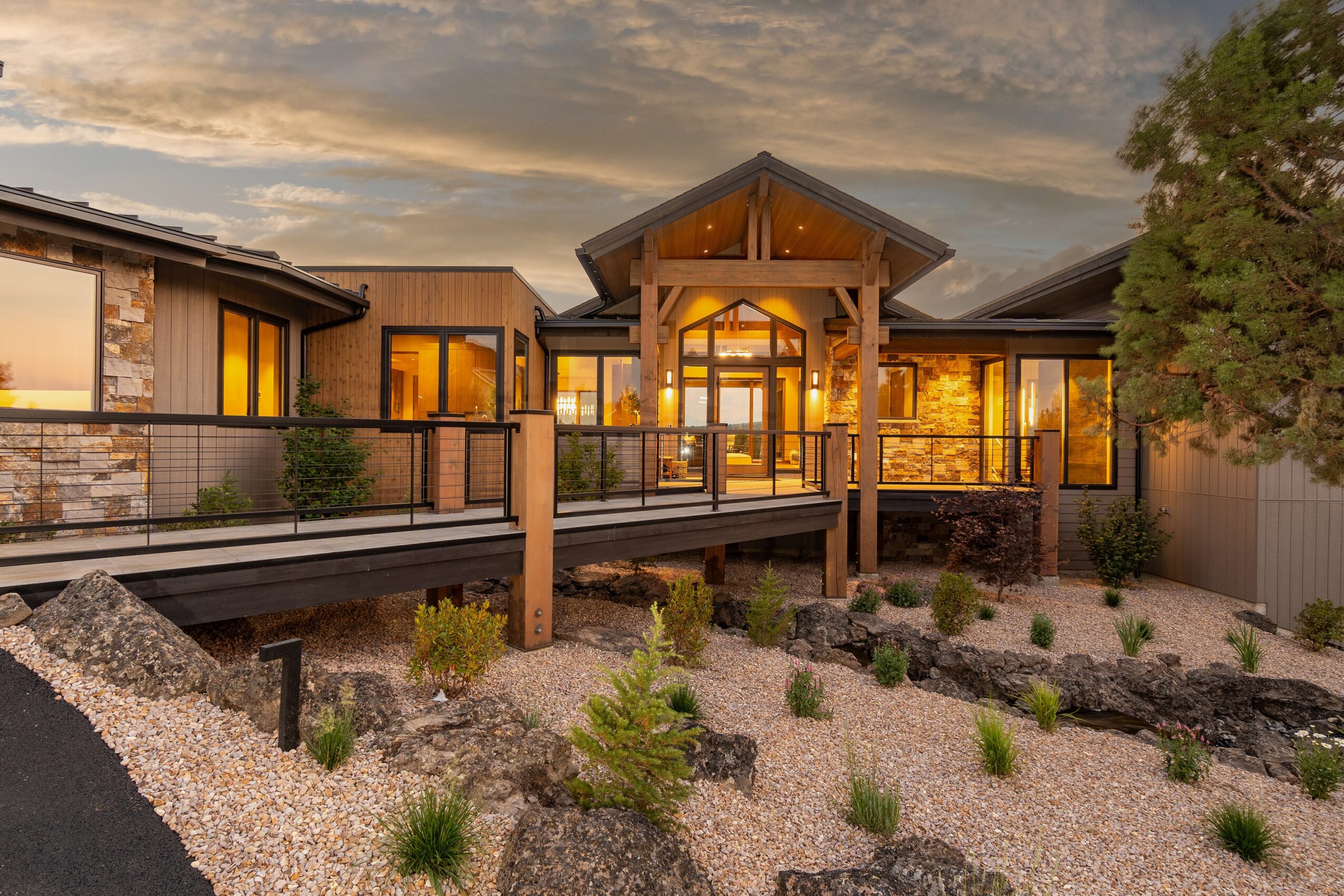 Modern house with large windows and a wooden entrance, surrounded by a landscaped yard with small plants and gravel.