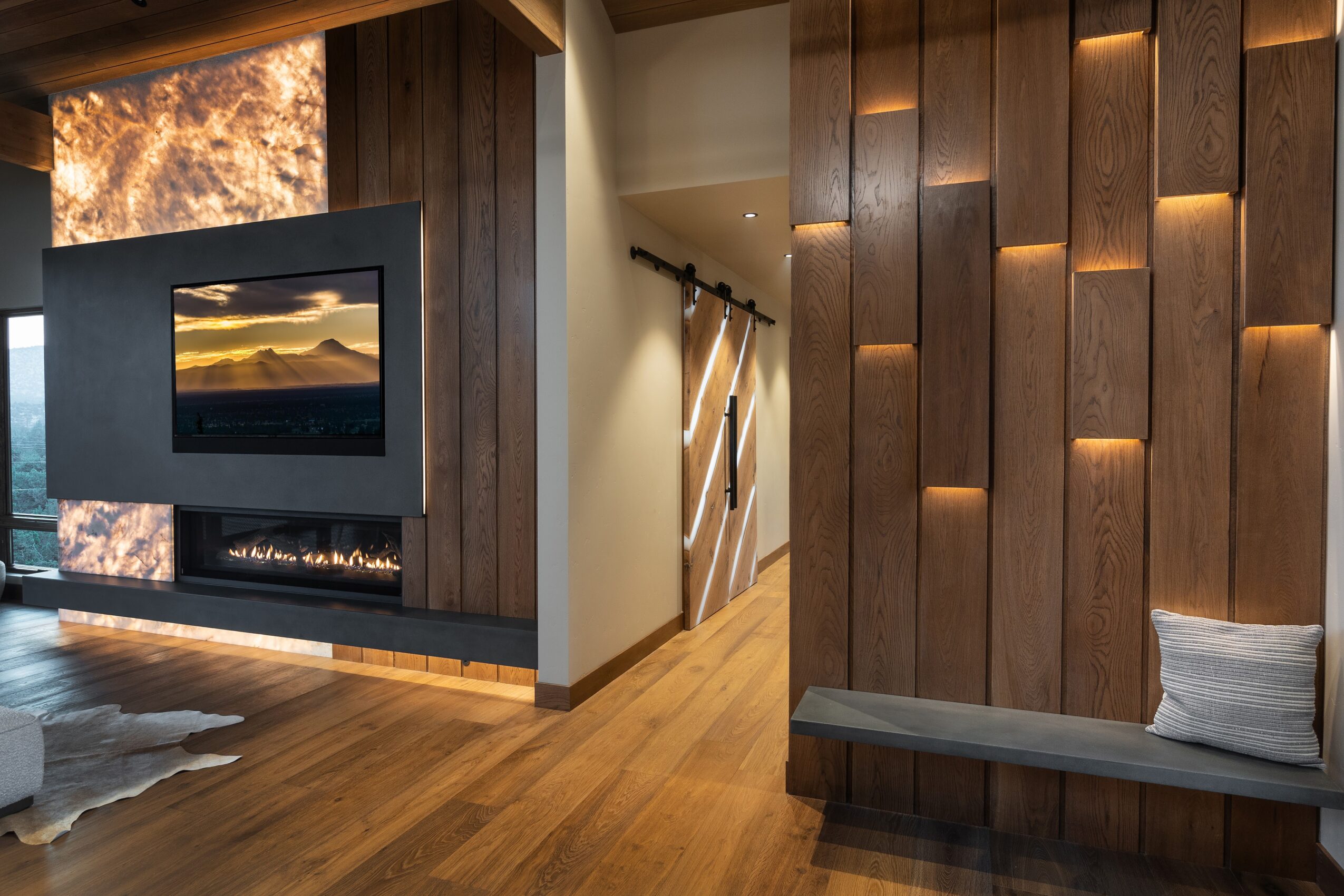 Modern living room with a wall-mounted TV, wooden paneling, and a cozy bench with a pillow, illuminated by warm lighting.