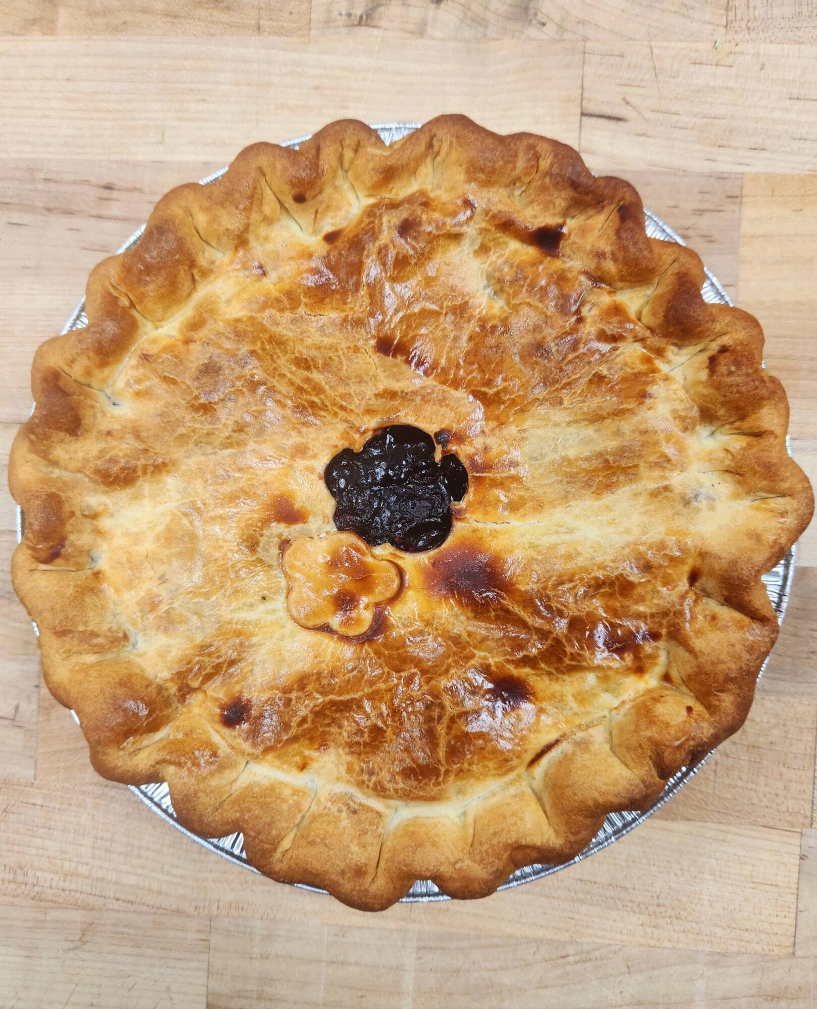 Round pie with a golden crust and a dark filling in the center, on a wooden surface.