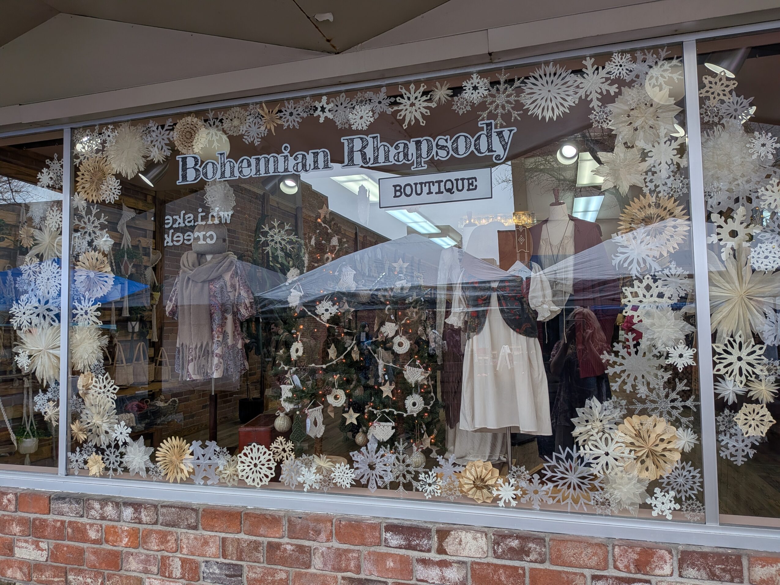 Store window decorated with snowflakes and flowers, displaying clothing and a sign for Bohemian Rhapsody Boutique.