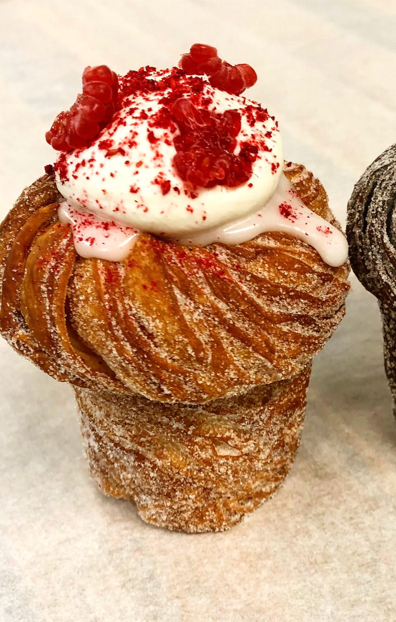 Pastry topped with whipped cream, red berries, and red crumbs, placed on a paper surface.