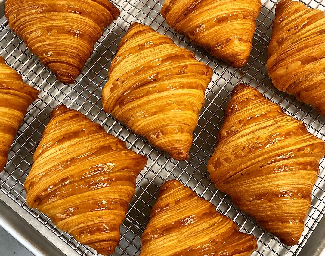 Golden-brown croissants on a wire rack, arranged in a pattern, with flaky layers visible.