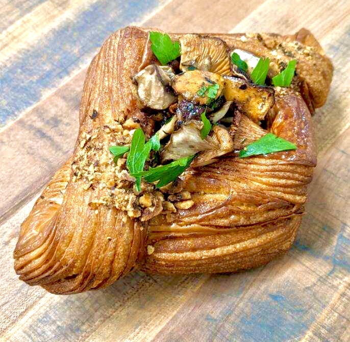 Pastry filled with meat and topped with green herbs on a wooden surface.