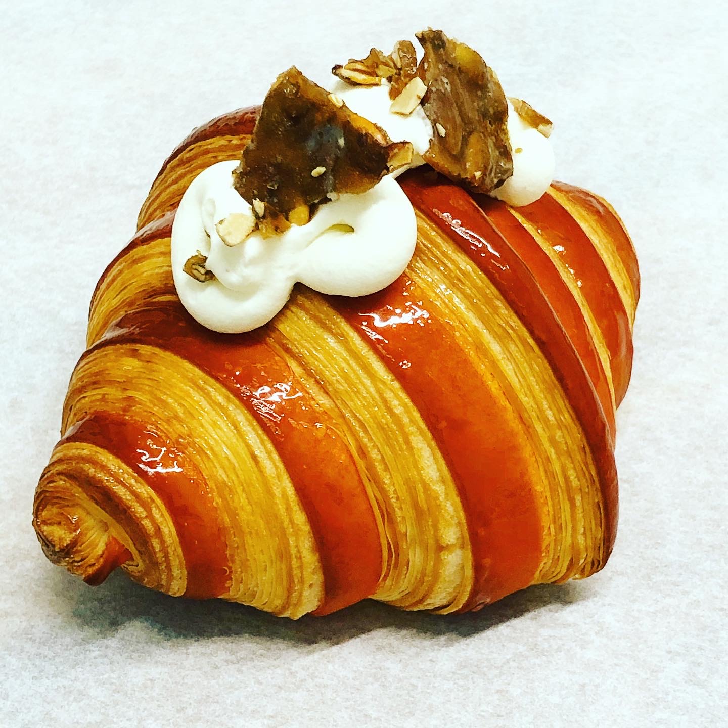 Croissant topped with whipped cream, caramelized nuts, and caramel drizzle, on a light background.