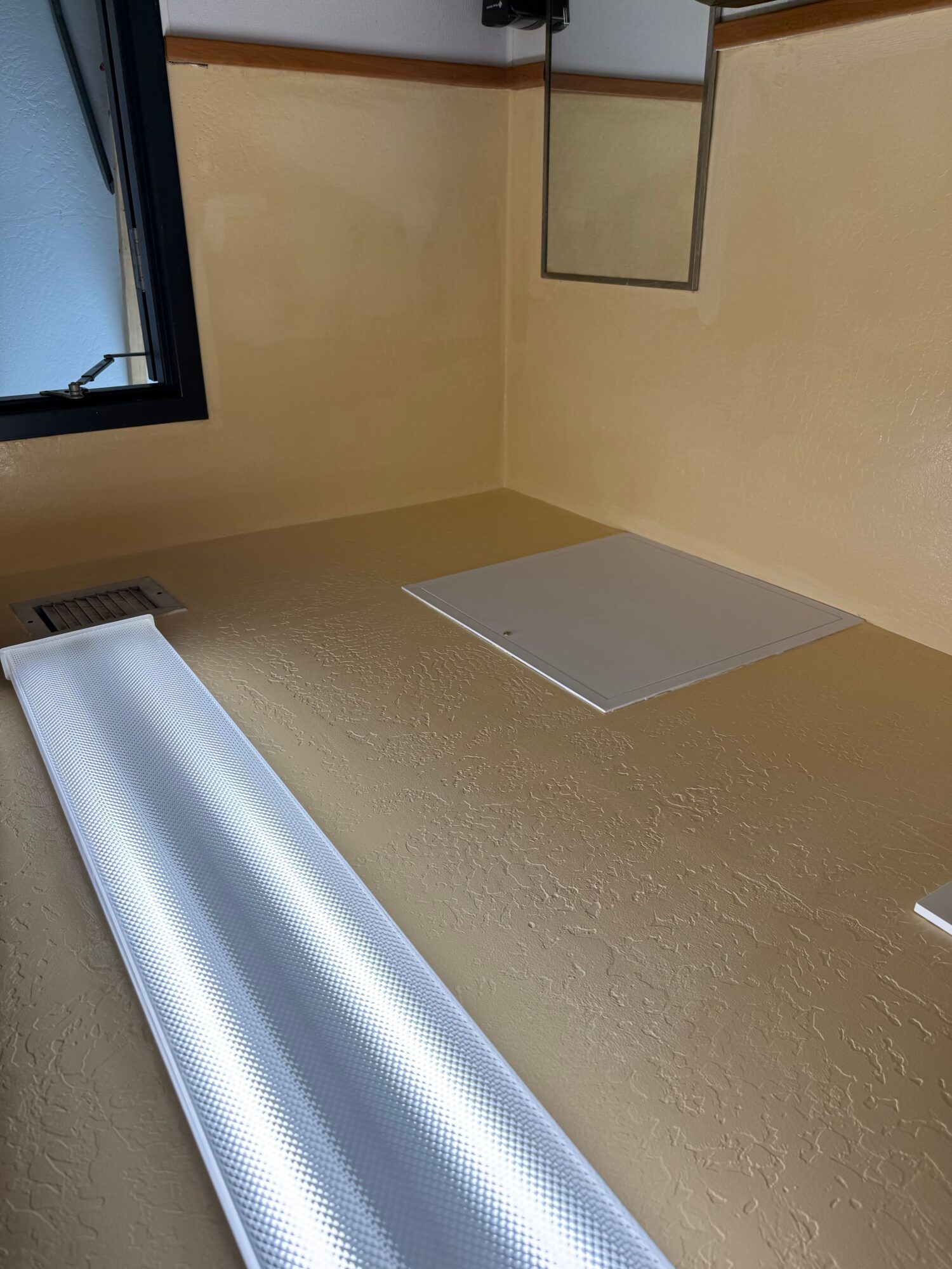 Ceiling with light fixture, vent, and window, viewed from below, with beige walls and ceiling.