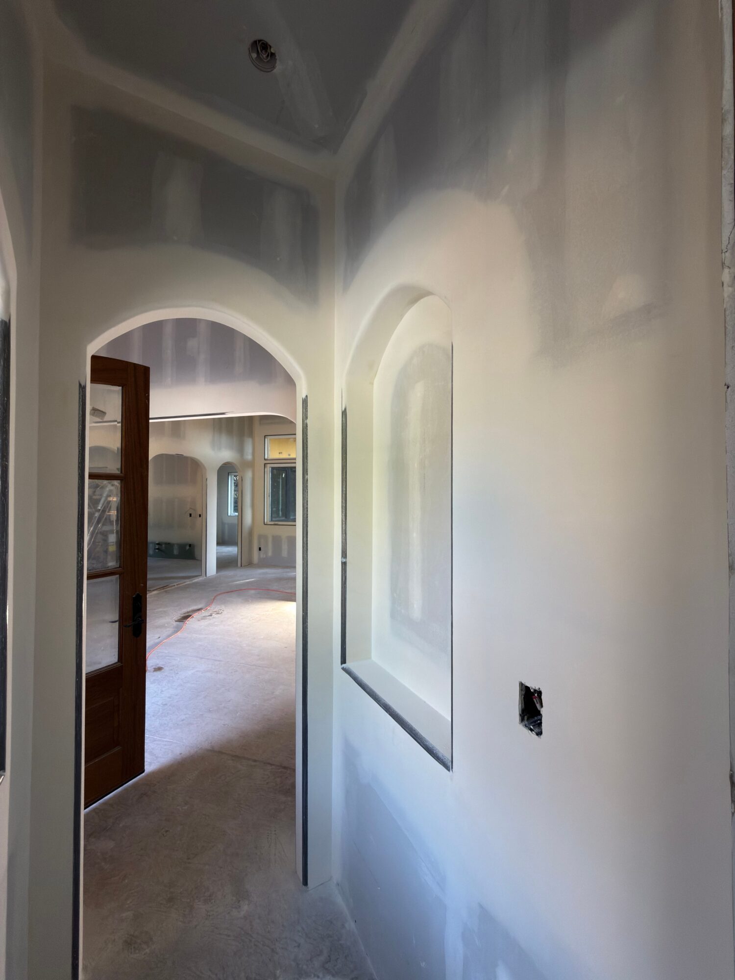 Interior view of a room with an arched doorway, ceiling light, and a partially visible door, with a hole in the ceiling.