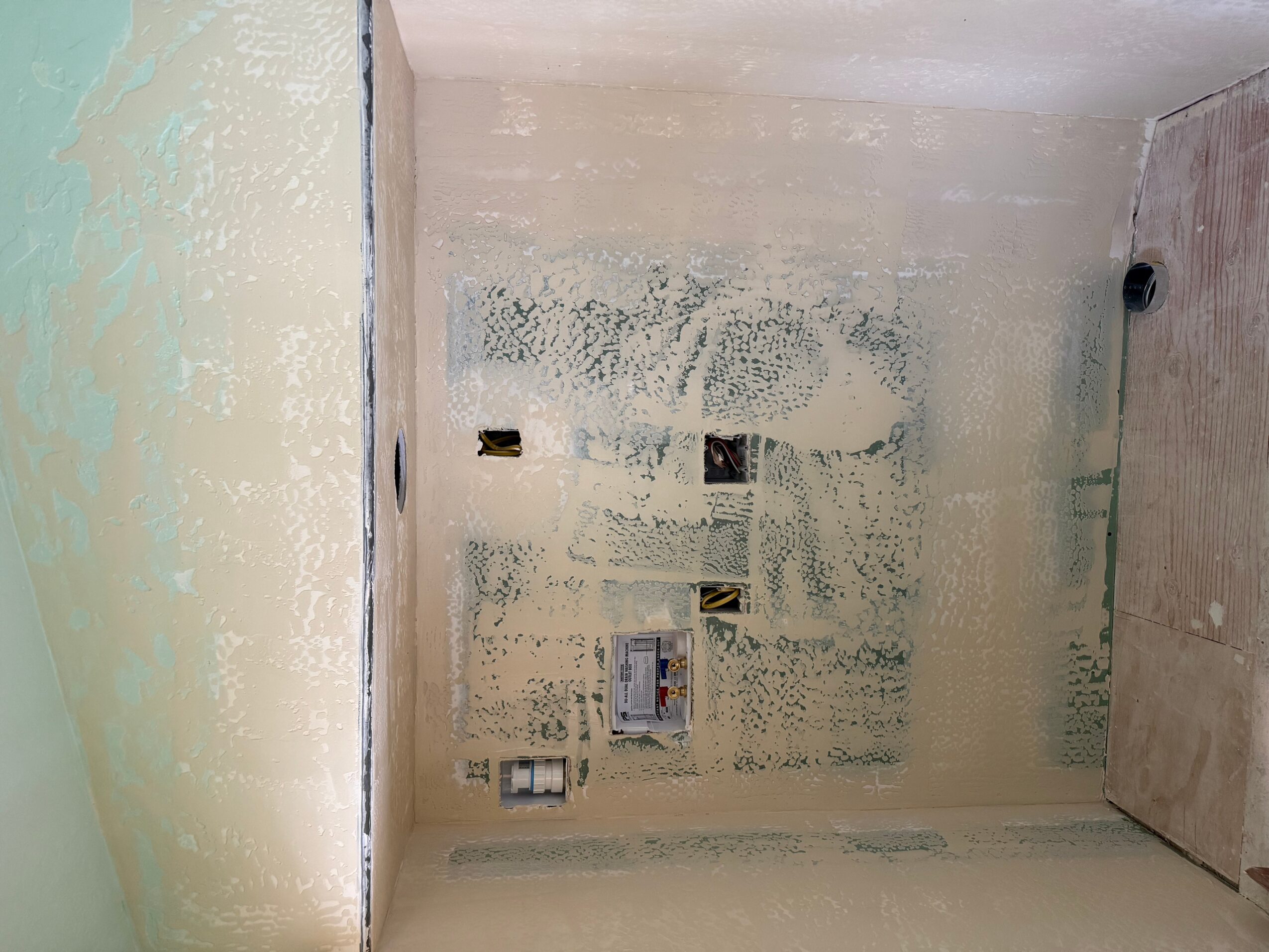 Room under construction with unfinished walls and exposed electrical outlets, viewed from the side, with construction materials visible.