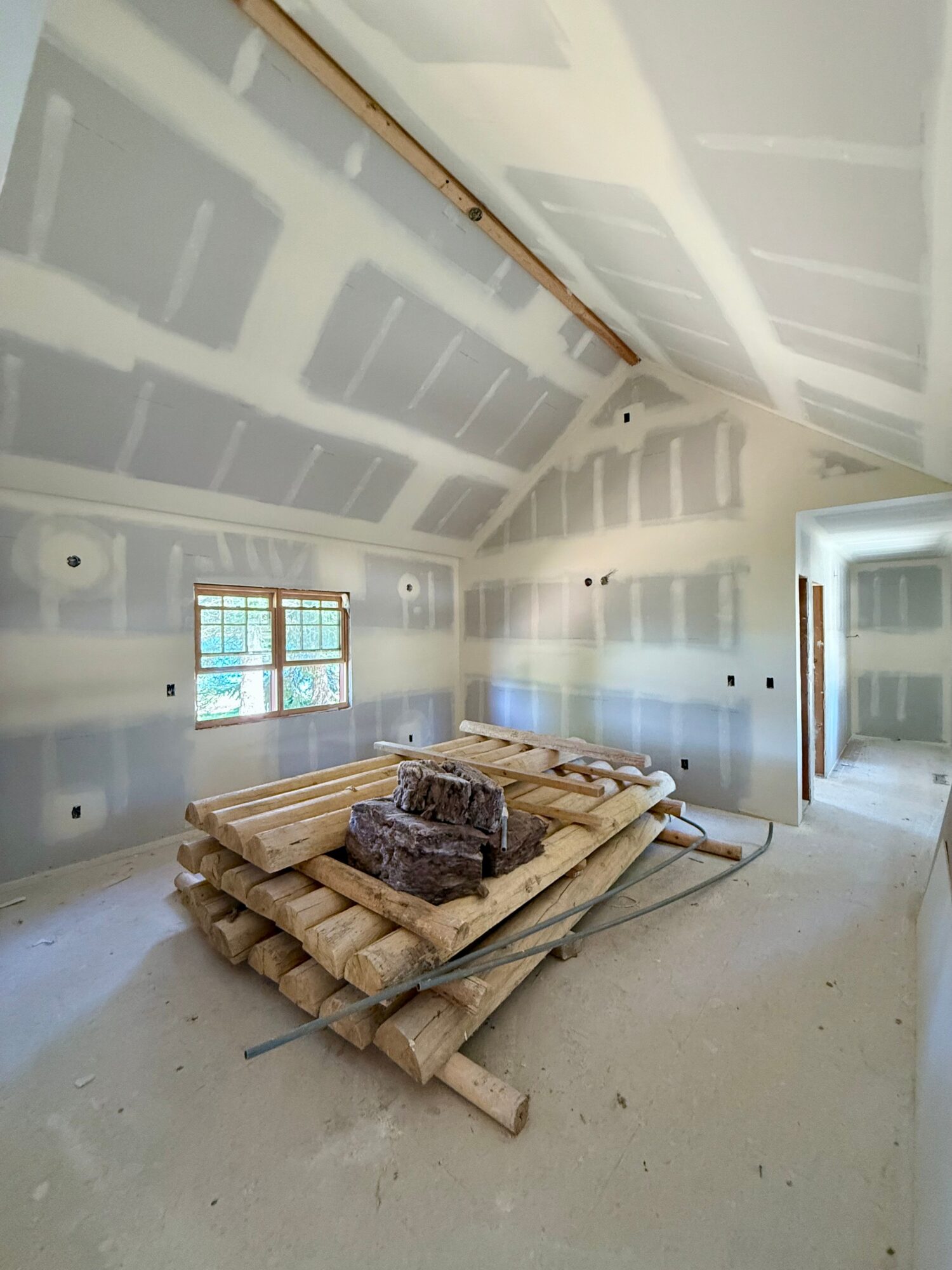 Room under construction with drywall on walls and ceiling, two windows, and construction materials on the floor.