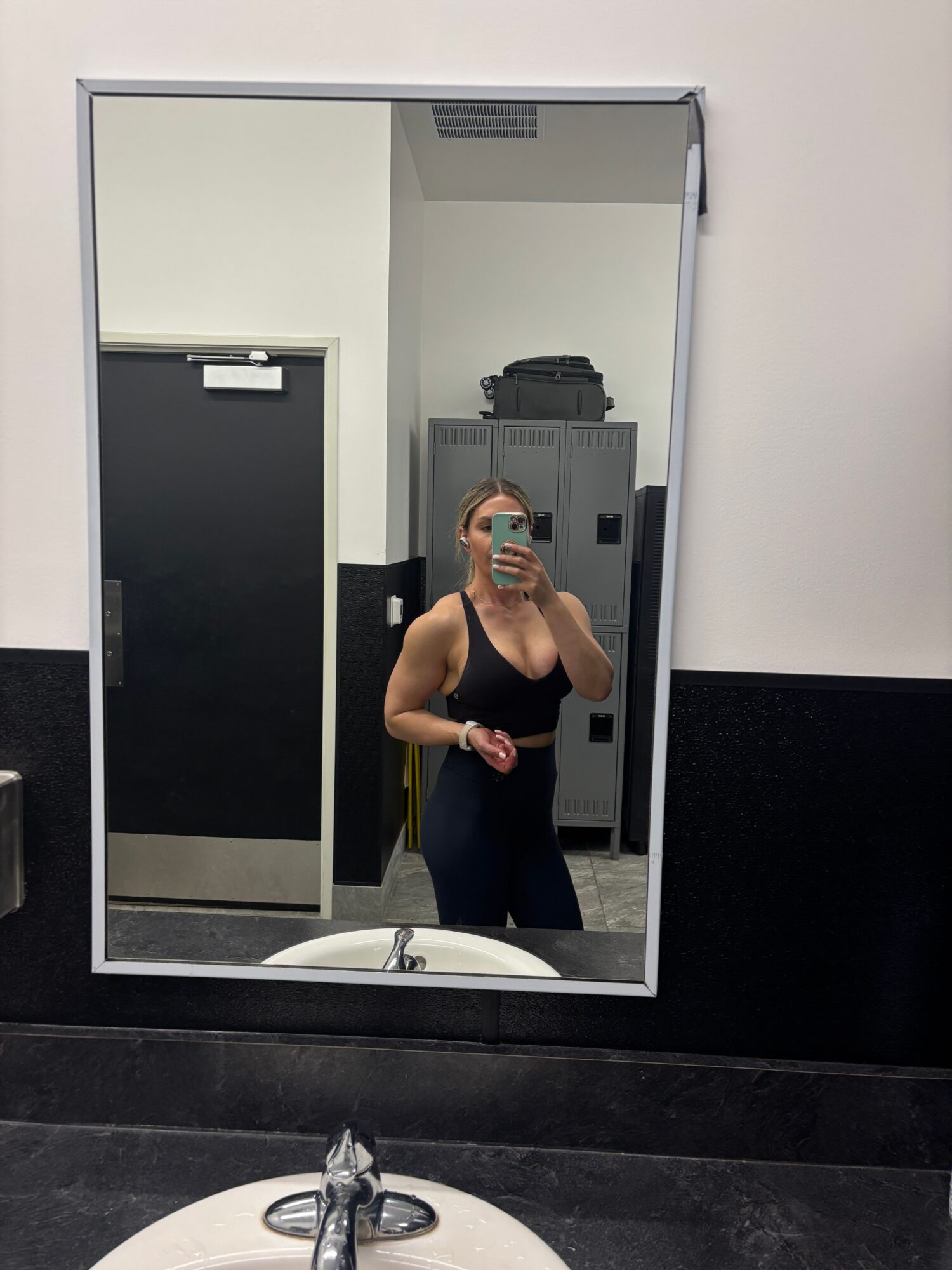 Person taking a mirror selfie in a bathroom, holding a phone, with a sink and black and white walls visible.