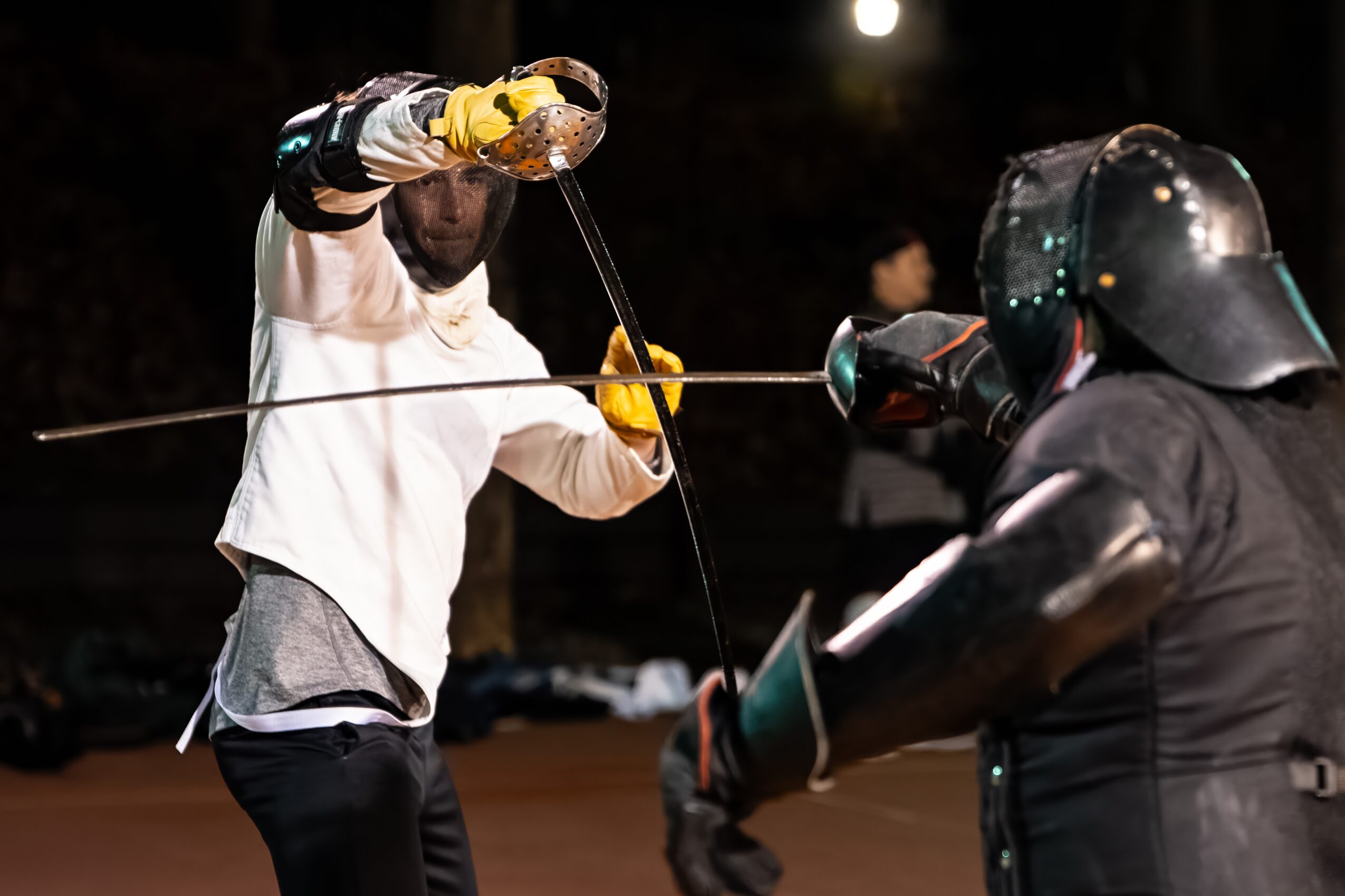 Fencer in white jacket and yellow glove prepares to strike another fencer in black protective gear during a match.