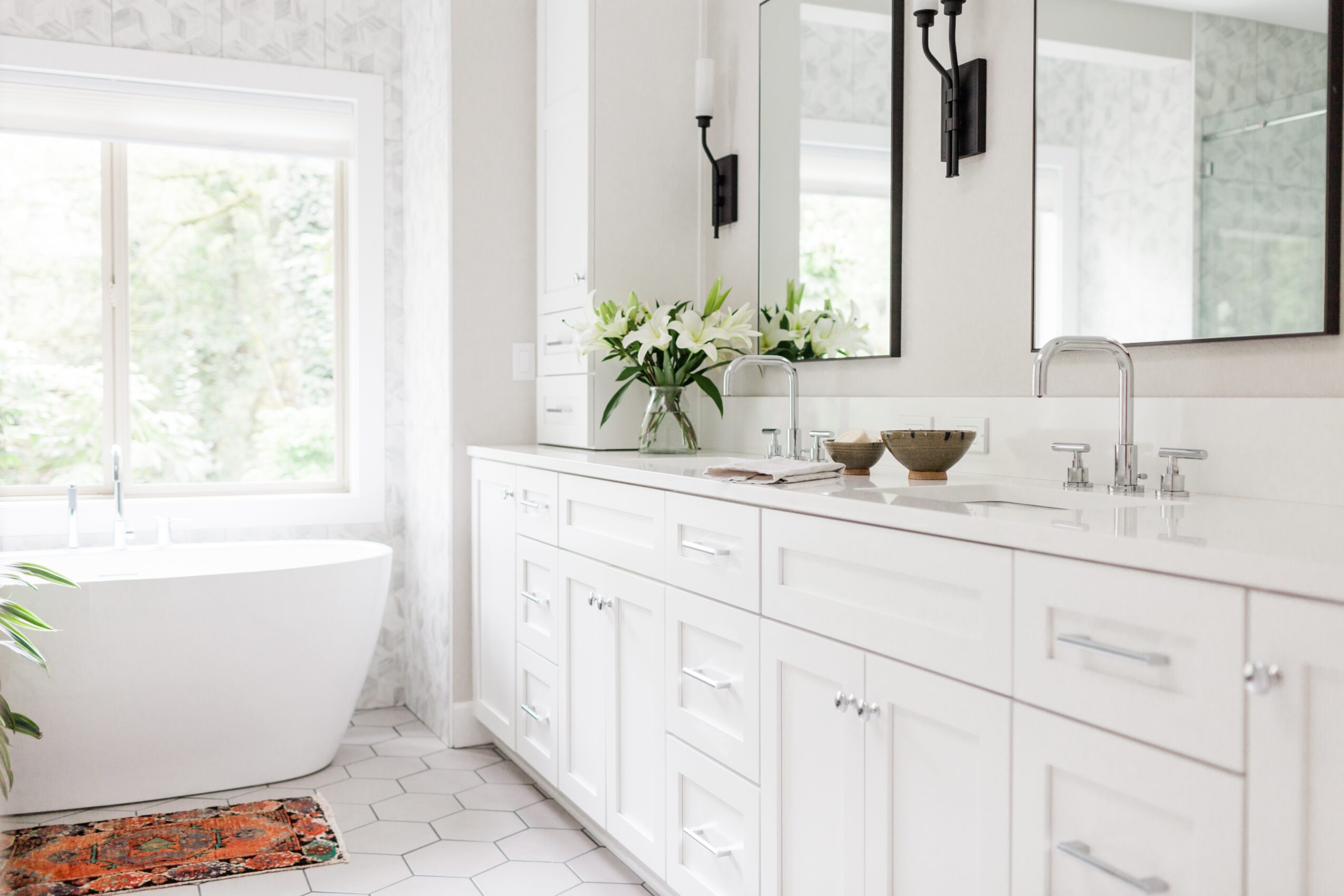 Bathroom with white vanity, large mirror, window, and a bathtub, decorated with plants and bowls, bright and airy.