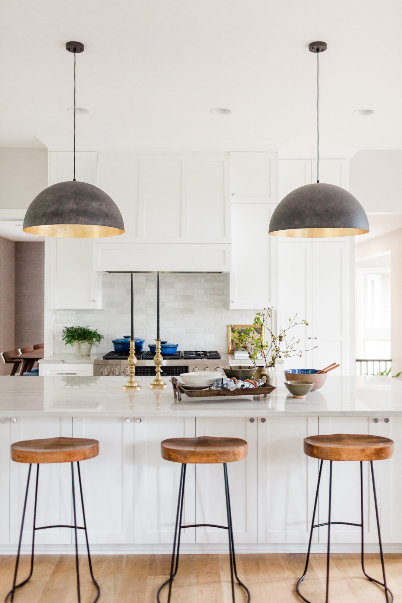 Kitchen with white cabinets, two pendant lights, three wooden bar stools, and a marble countertop.