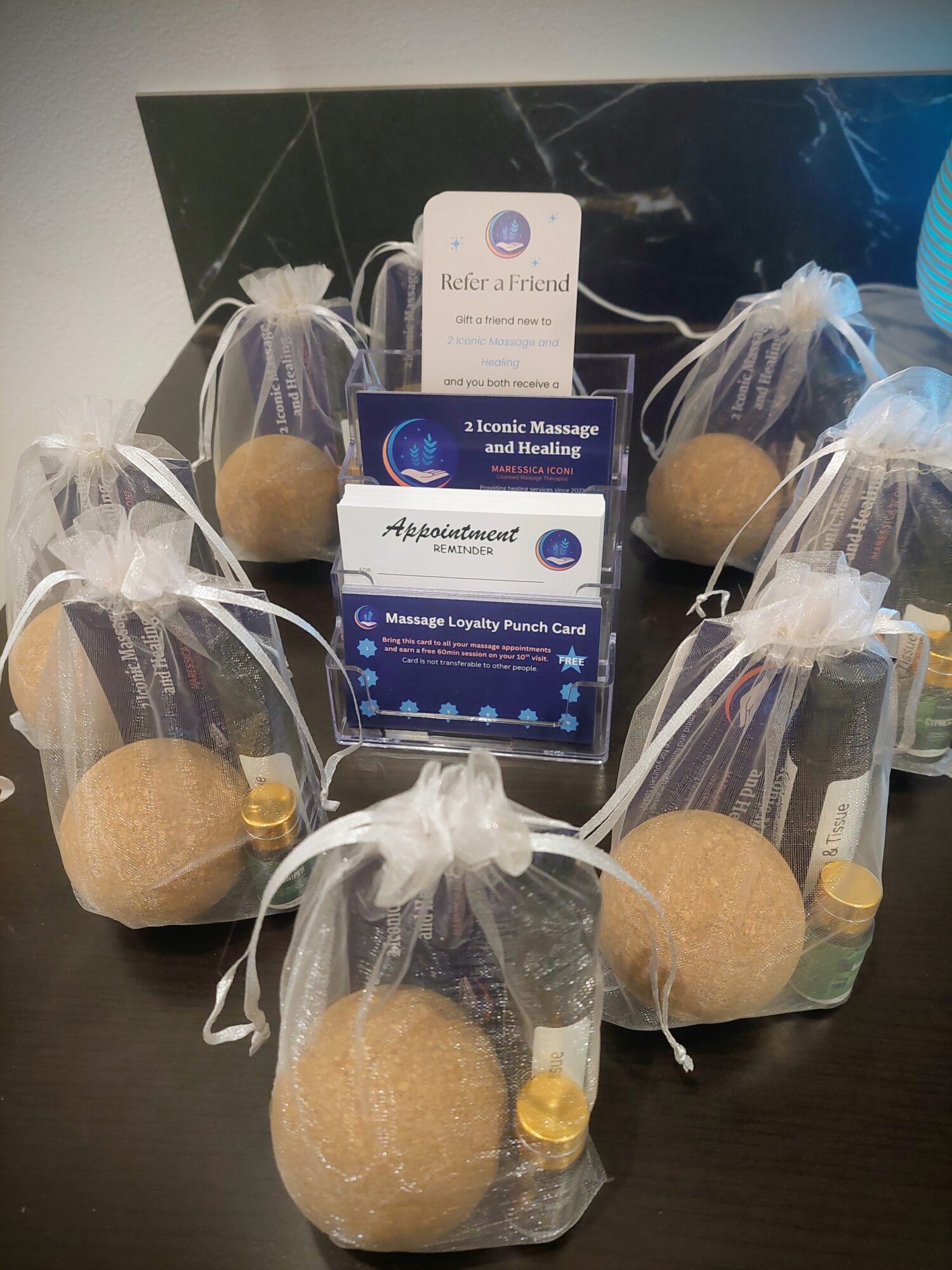 Five gift bags with bath bombs and small bottles, arranged on a dark surface, with a black background.