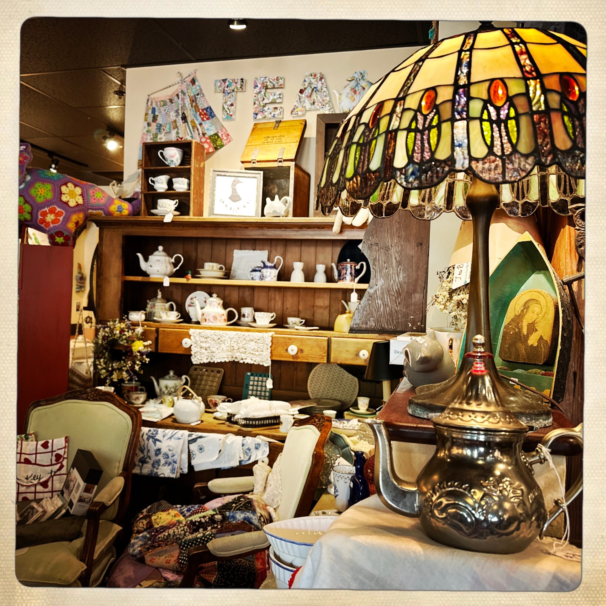 Display of vintage teapots, a stained glass lamp, and various furniture and decorative items in a store.