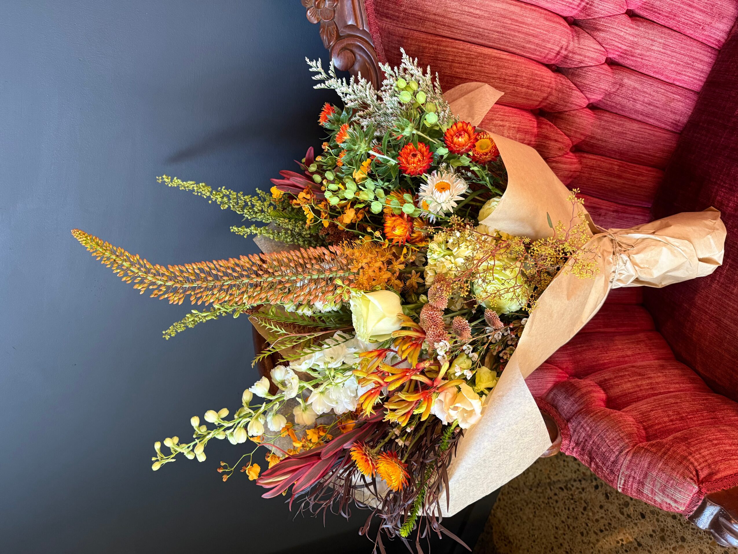 Colorful bouquet of flowers with various blooms and greenery, resting on a red upholstered chair.